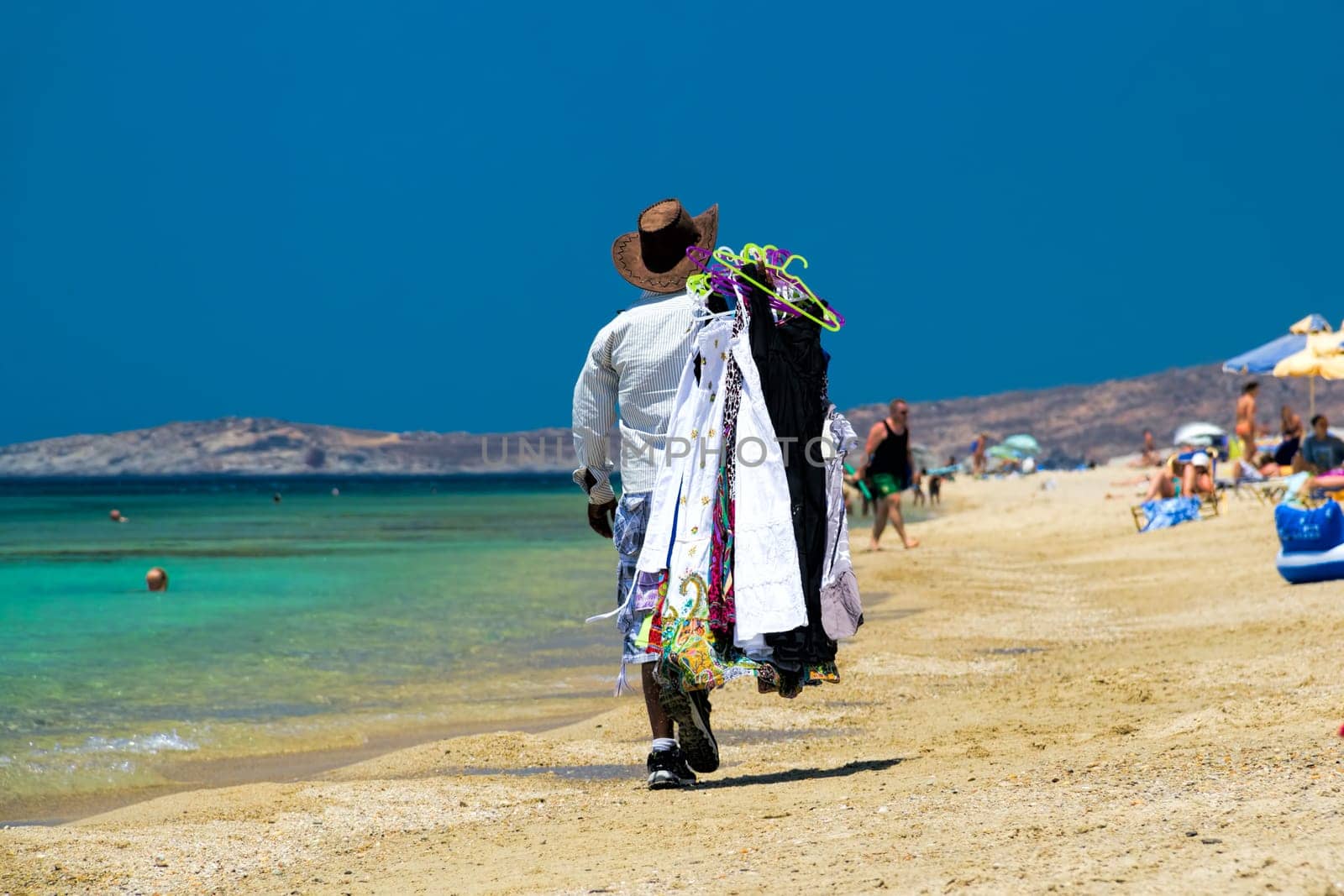 Back view of a man walking along the beach carrying clothes, Maragas (Plaka) beach, Naxos island, Cyclades, Greece