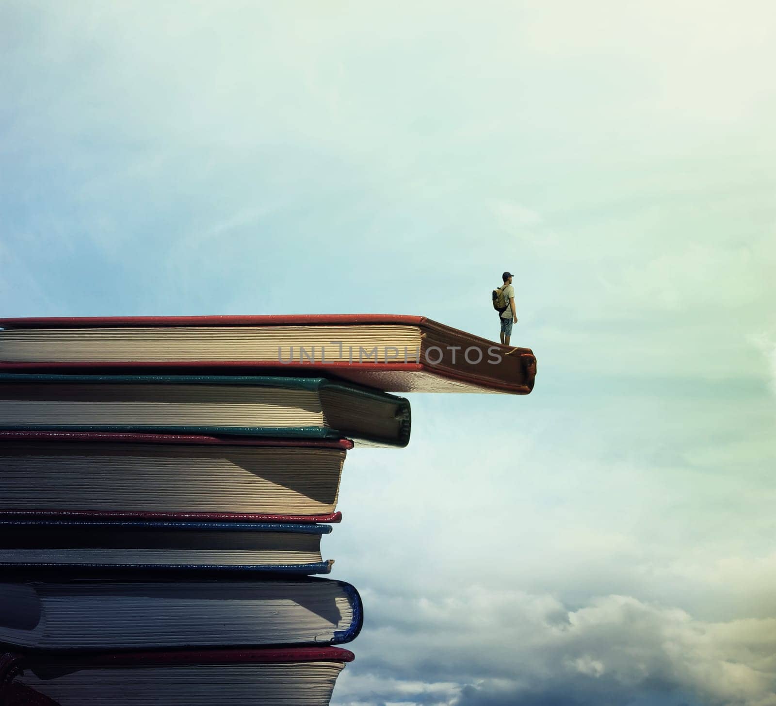 Young boy with a bag on his back stand on a stack of books looking far at horizon. In search of knowlegde concept.