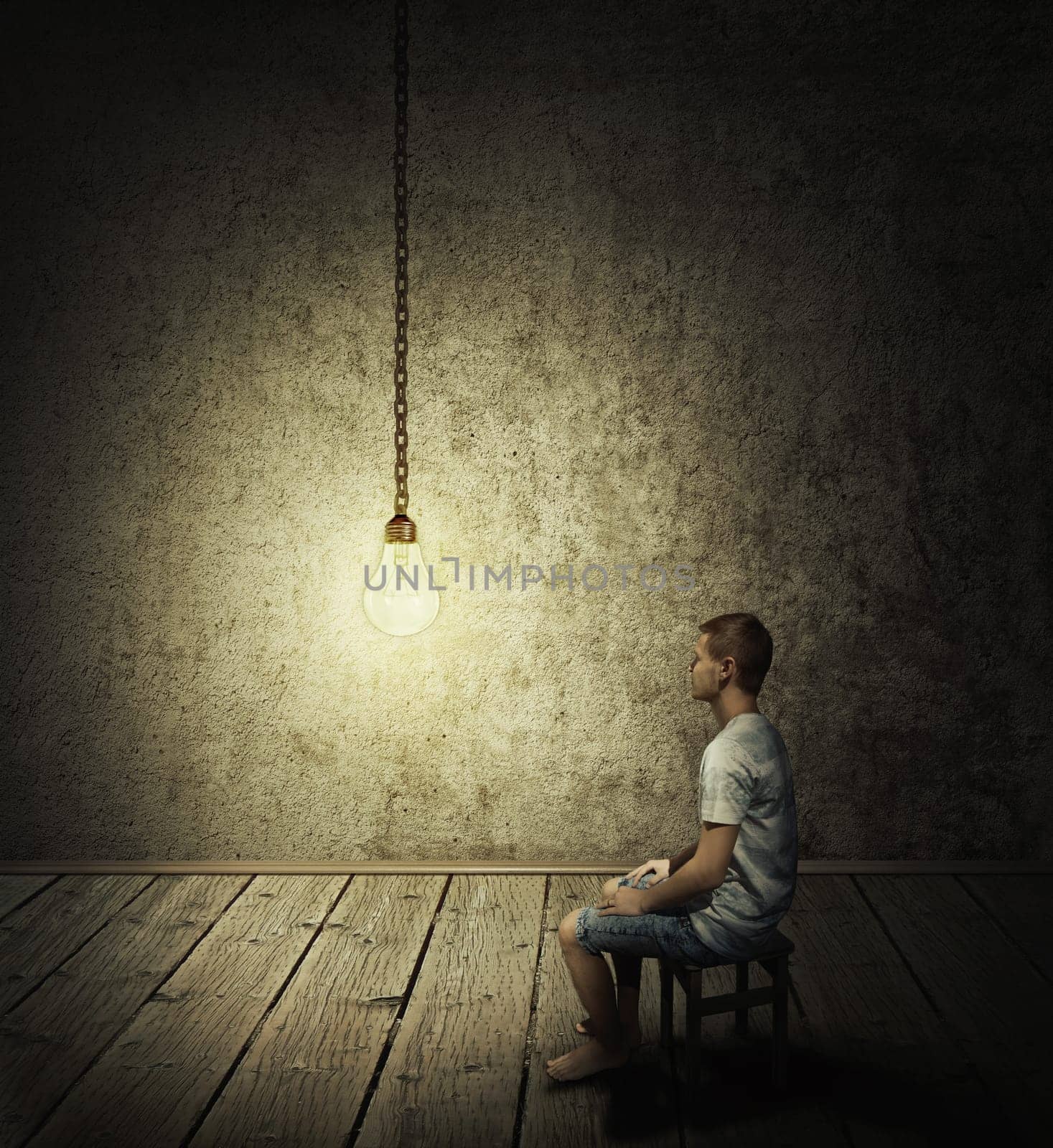 Creative idea concept with a man sitting in a dark room, looking at a lightbulb