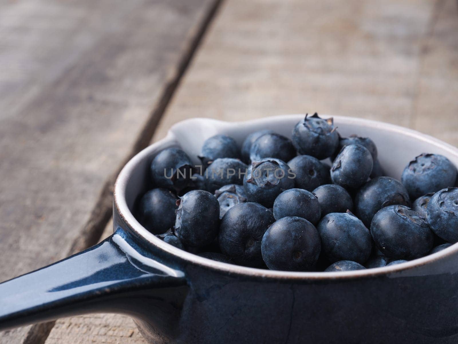 Fresh organic blueberries in a rustic blue bowl on old wooden plank