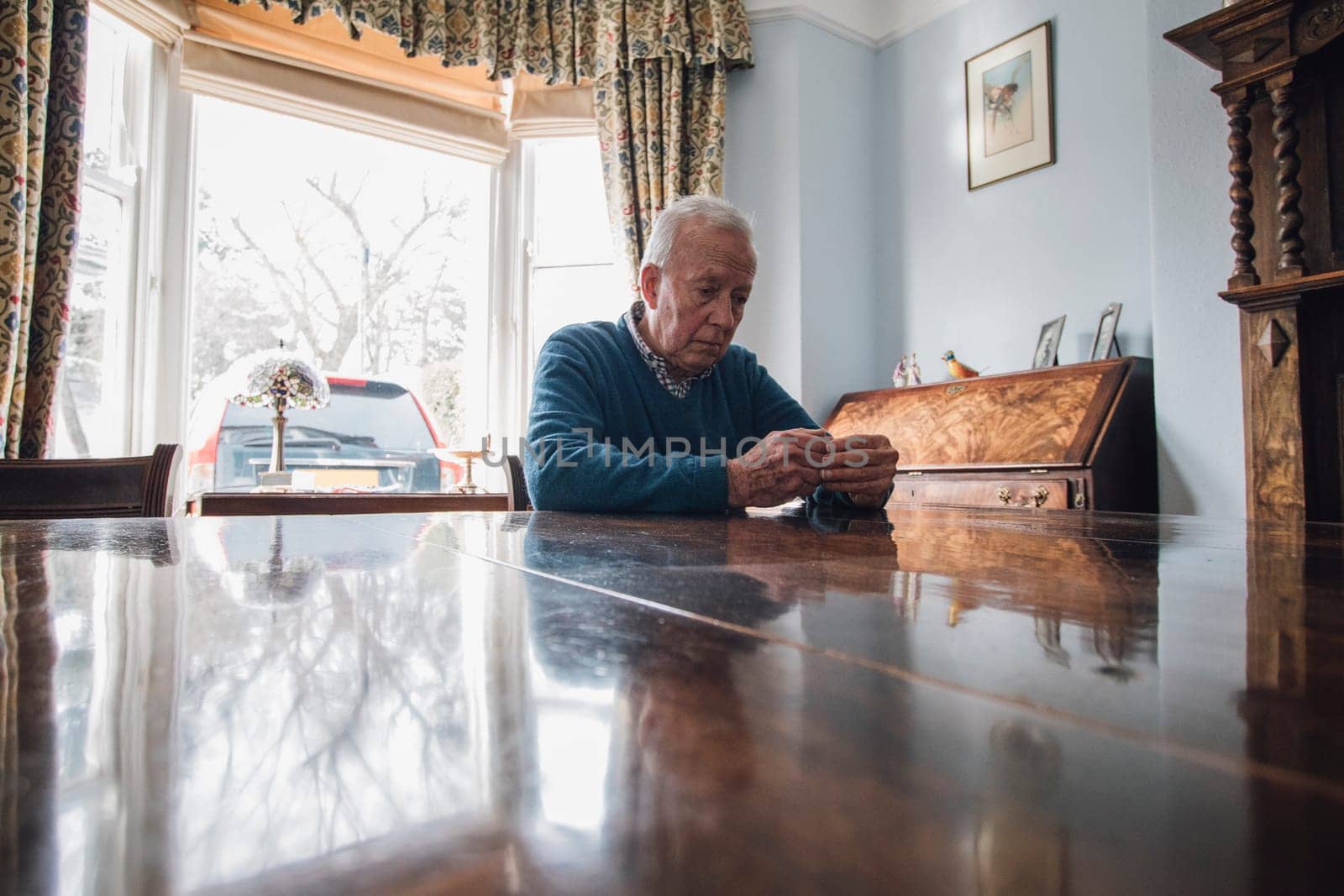 Senior man is sitting alone at the dining table in his home, with a worried expression on his face.