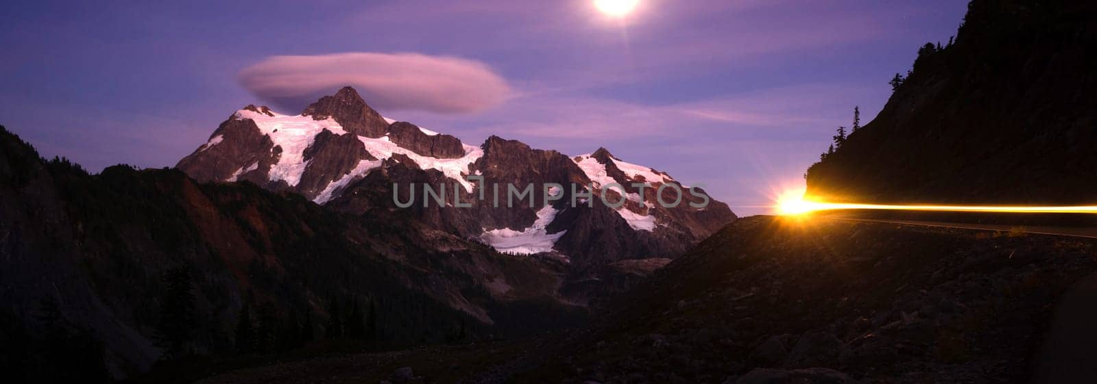 The moon lights up the mountainside as a car creates light streaks in this long exposure