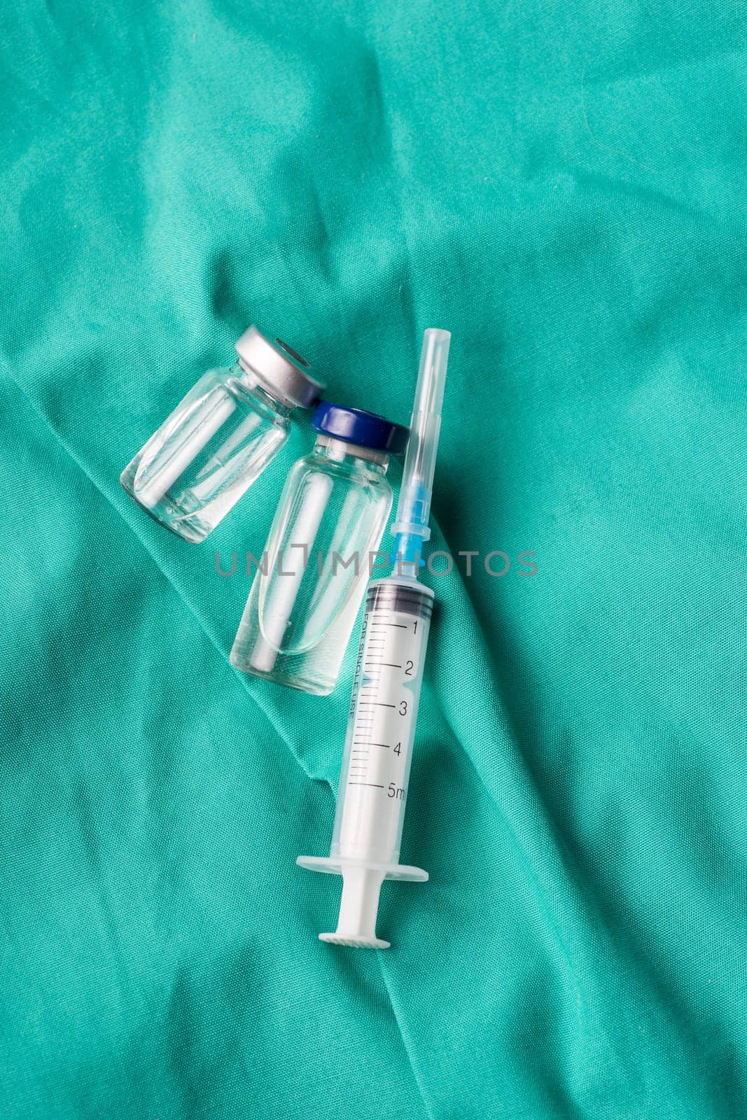 Medical syringe and vials lying on the hospital's green background. The background can be a textile part of a doctor or nurse's work uniform