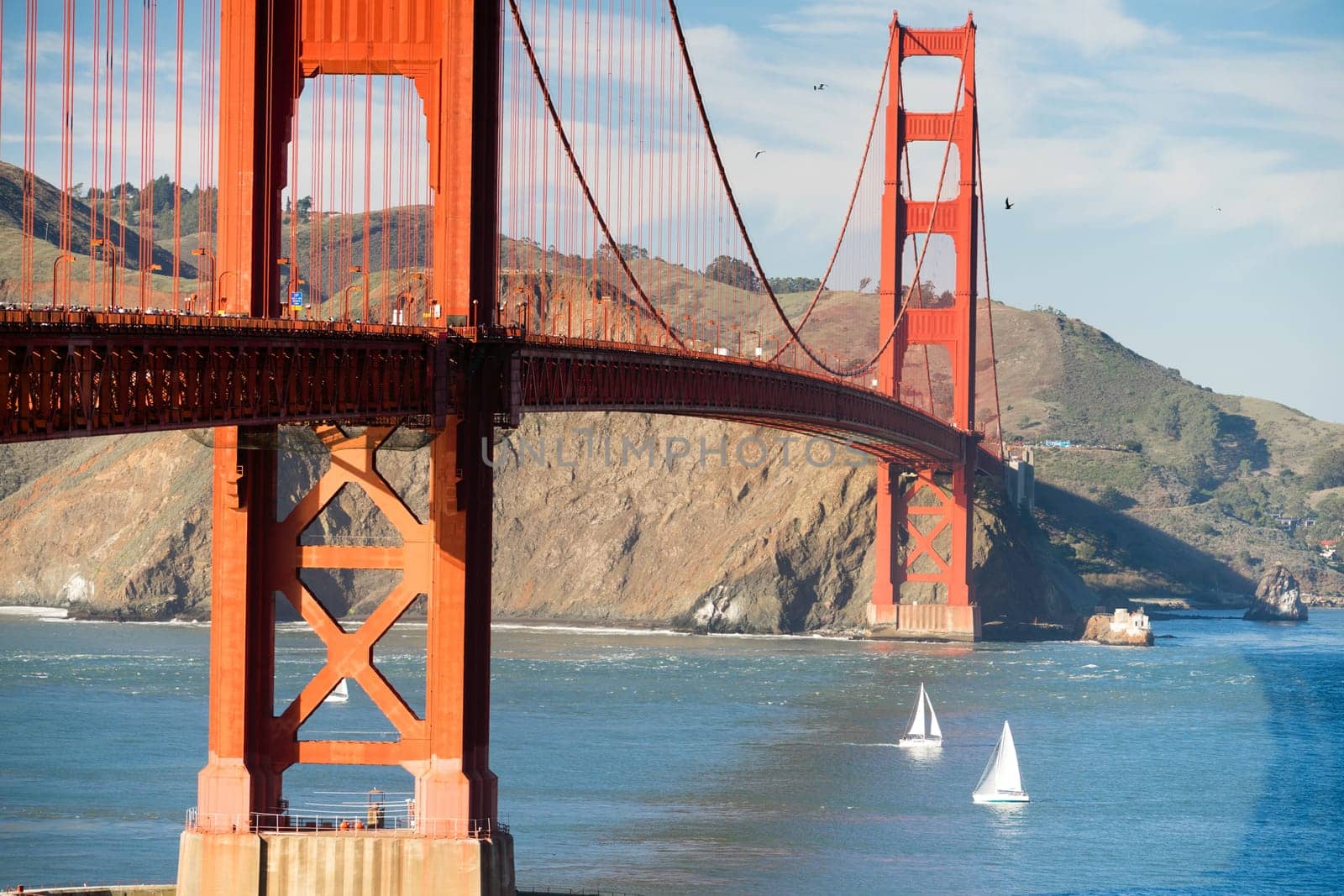 Sunset is on the way as cars, pedestrins, boats, and birds move around the Golden Gate Bridge