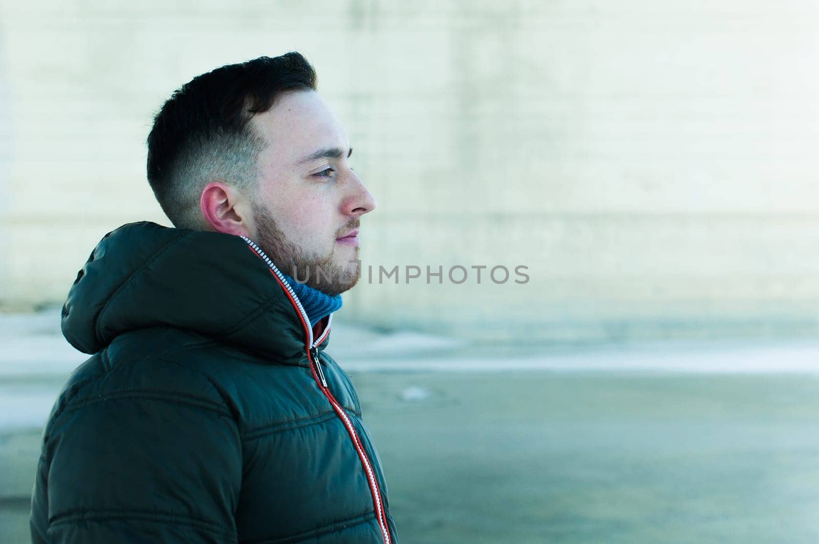 man in warm clothes with a beard is walking on the street in the winter in a warm sunny day at the river bridge in the background