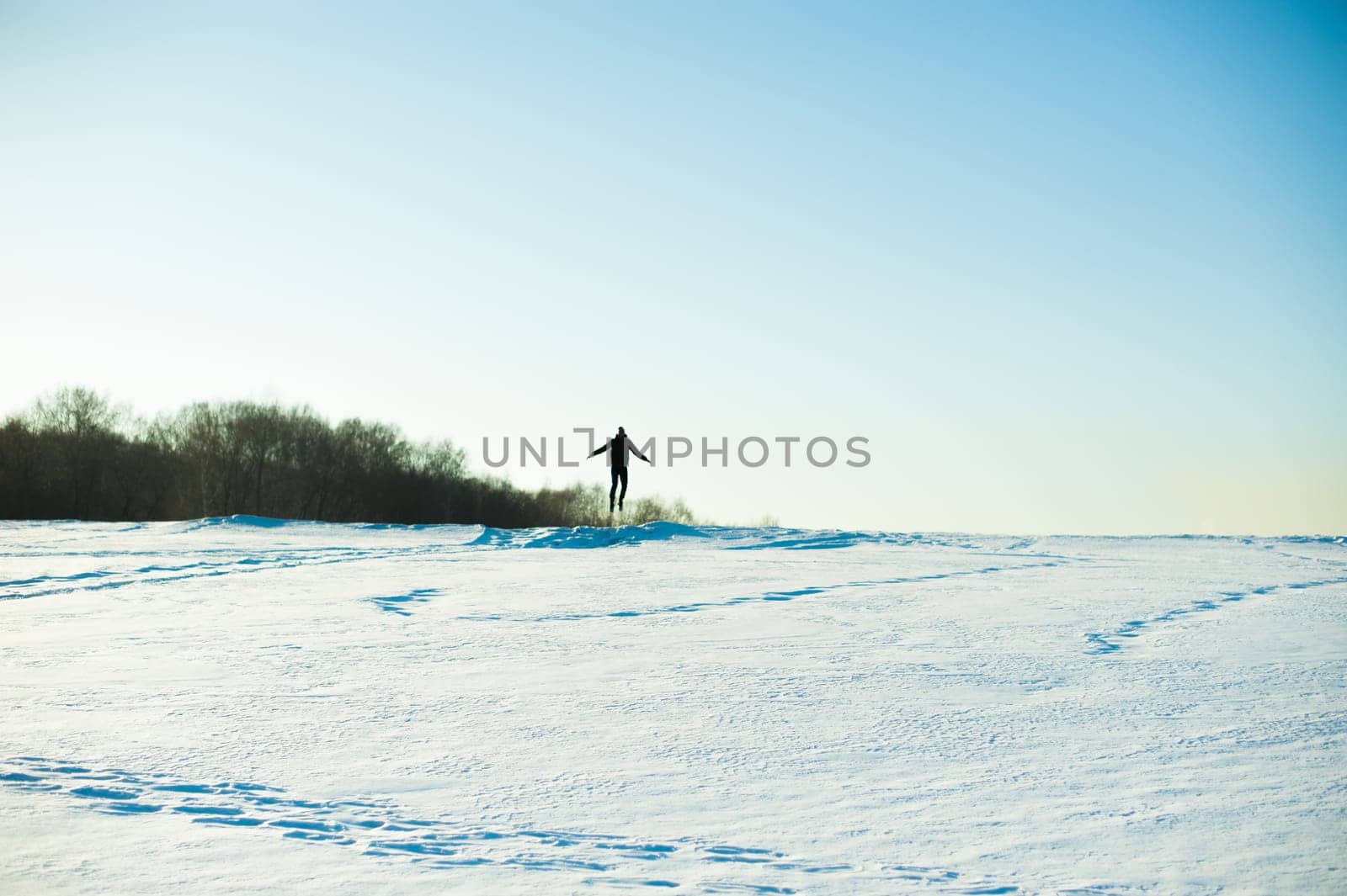 man in warm clothes with a beard is walking on the street in the winter in a warm sunny day at the river against the sky, jumping up and running in the snow