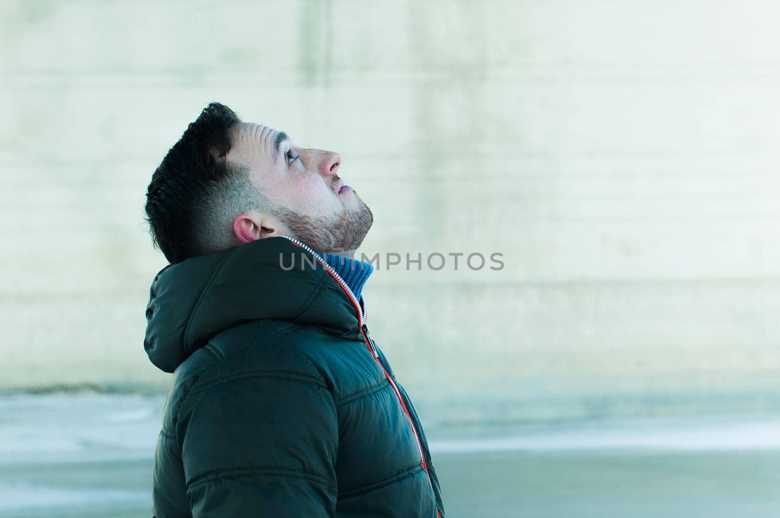 man in warm clothes with a beard is walking on the street in the winter in a warm sunny day at the river bridge in the background