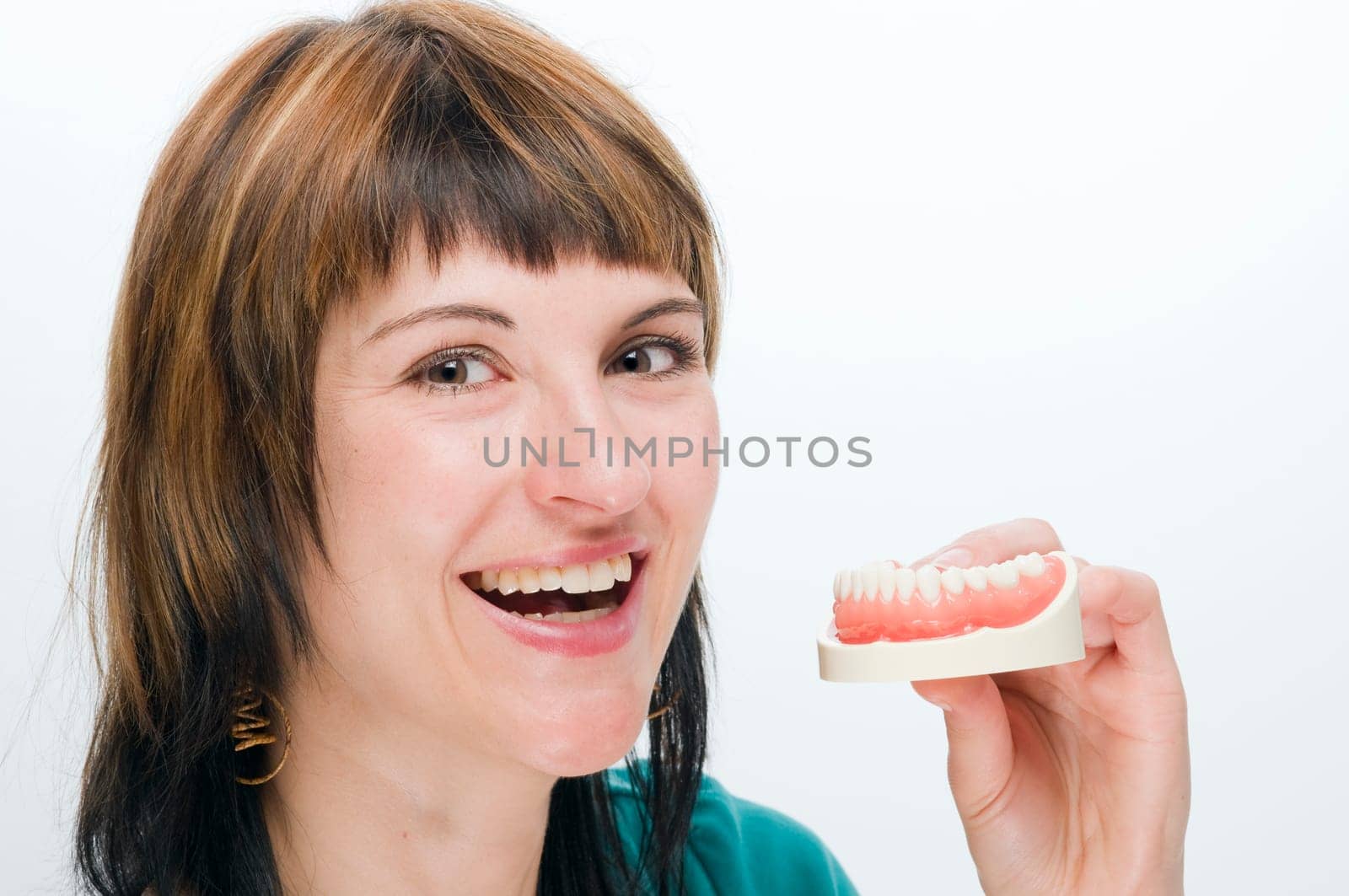 Lateral head portrait of a young laughing woman with prosthesis held in front of her teeth against a white background