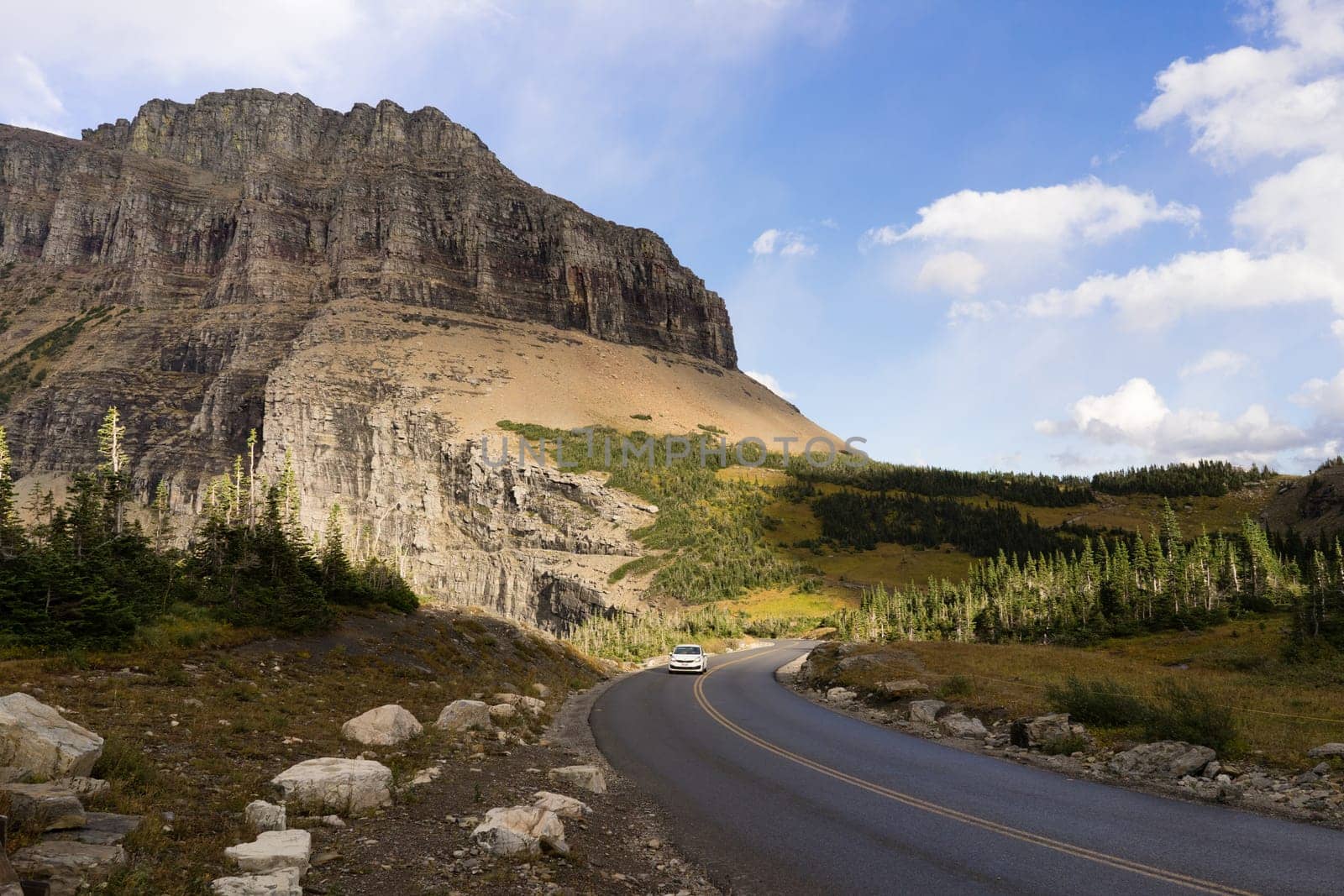A lone white car makes a curve under the tall peaks of the Rocky Mountains