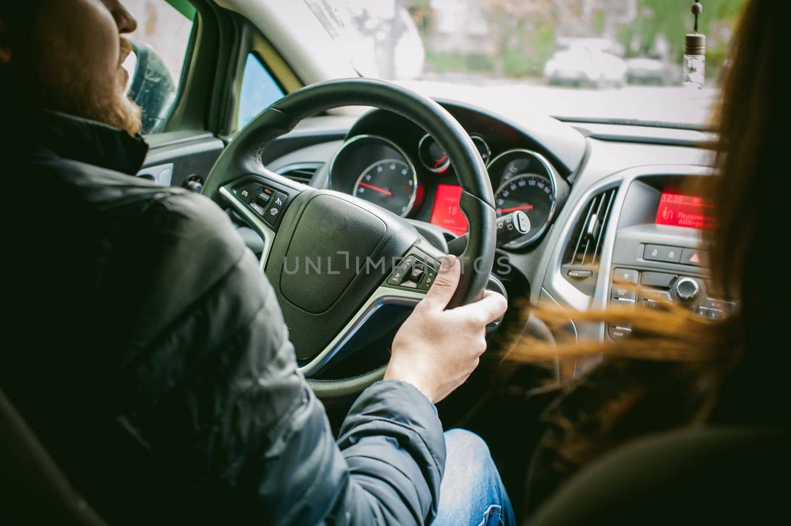 man drives a car. A guy in a jacket sits behind the wheel of a car traveling on the road in a traffic jam. Photo taken off the seat, due to the driver's back