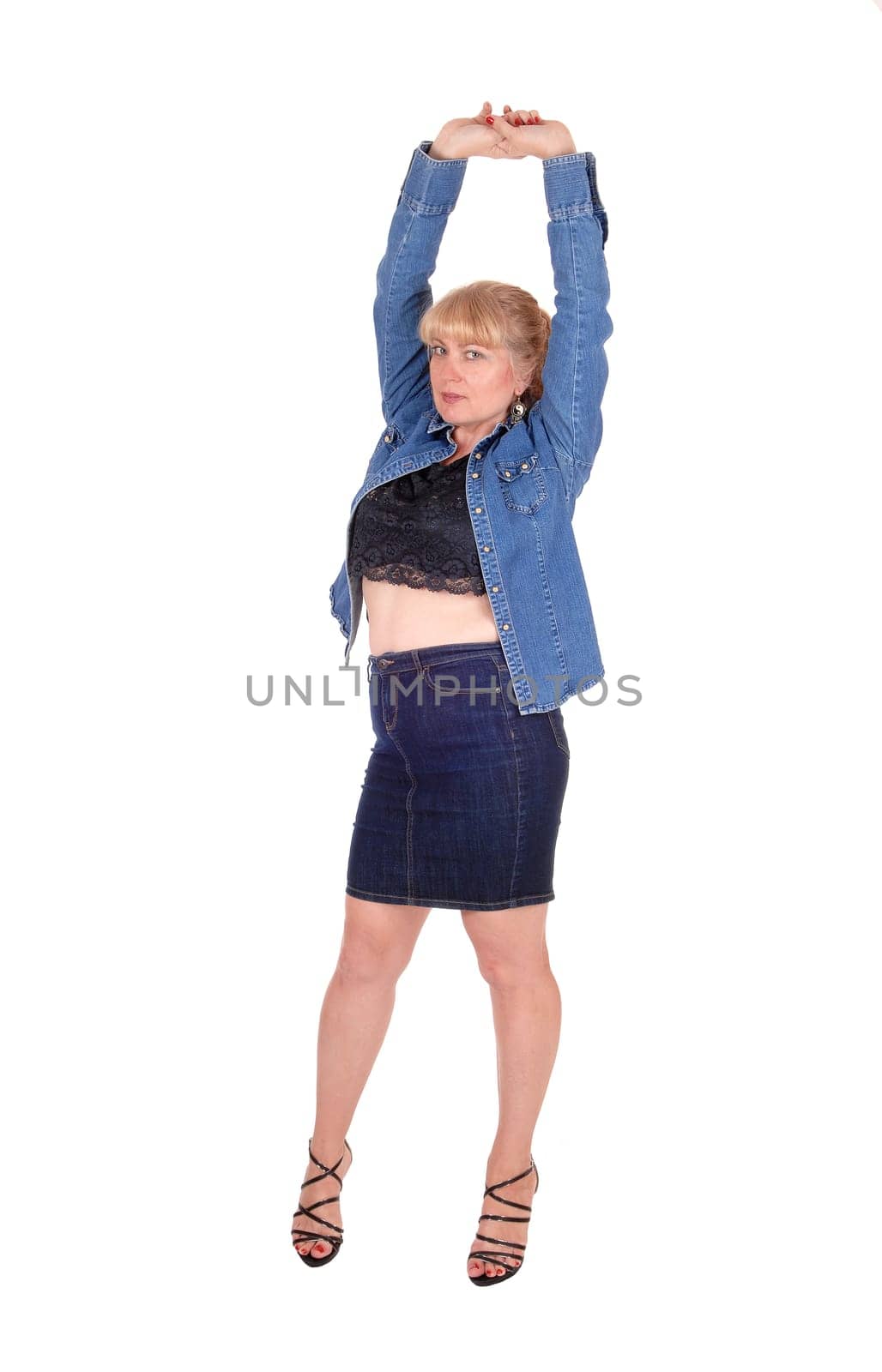 A beautiful blond woman standing in a jeans jacket and skirt with her.arms stretched up, isolated for white background..