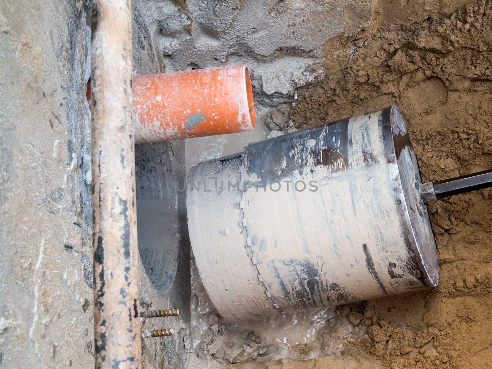 View of a finished core hole borehole with drill bit and drill core in a dug trench in front of a concrete wall.