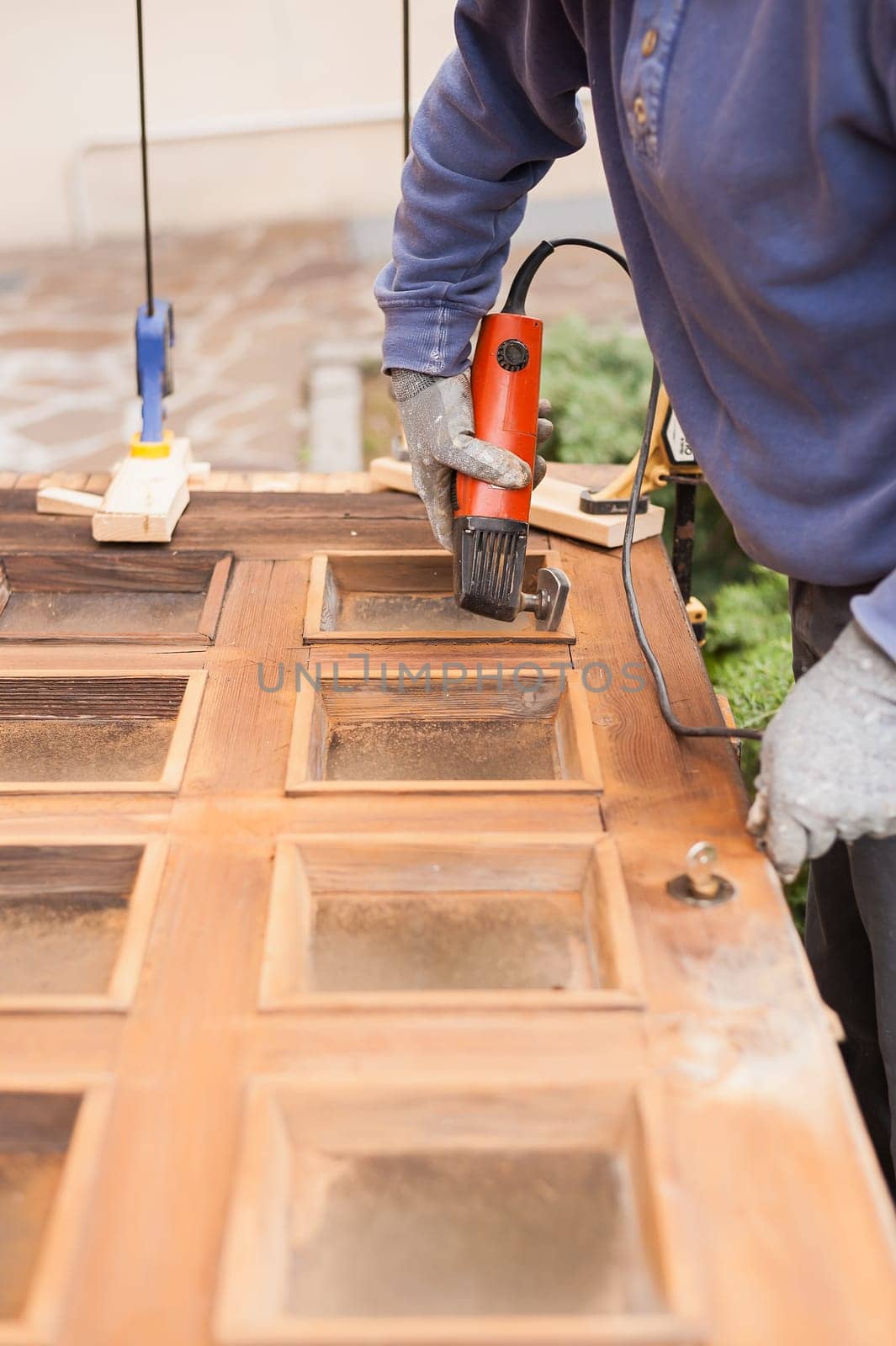 Carpenter at work with angular Sander. Maintenance and restoration of an old wooden door.