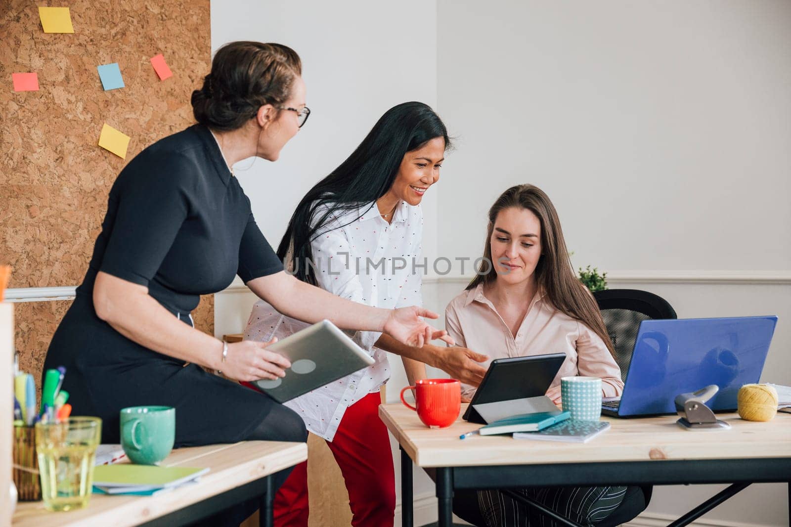 Women are working together in an office. They are talking as they use digital tablets.