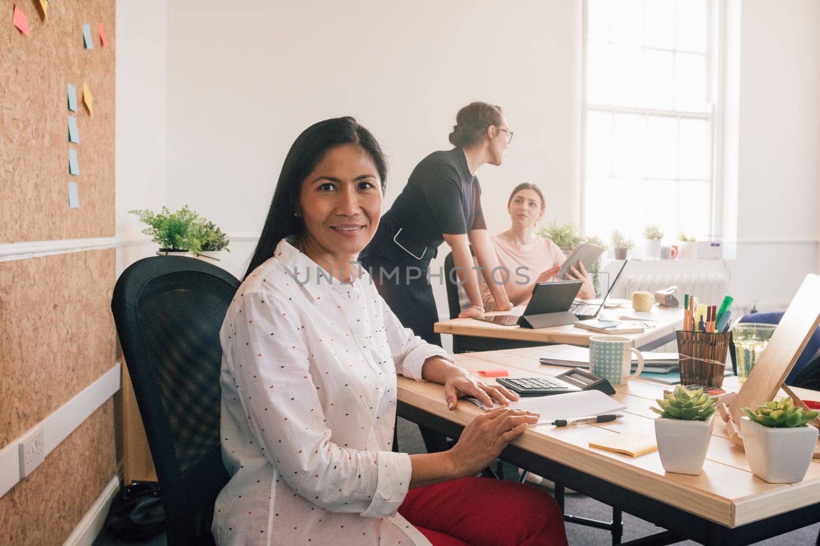 Portrait of a female employee in her workplace. She is sitting at her desk and is smiling at the camera.
