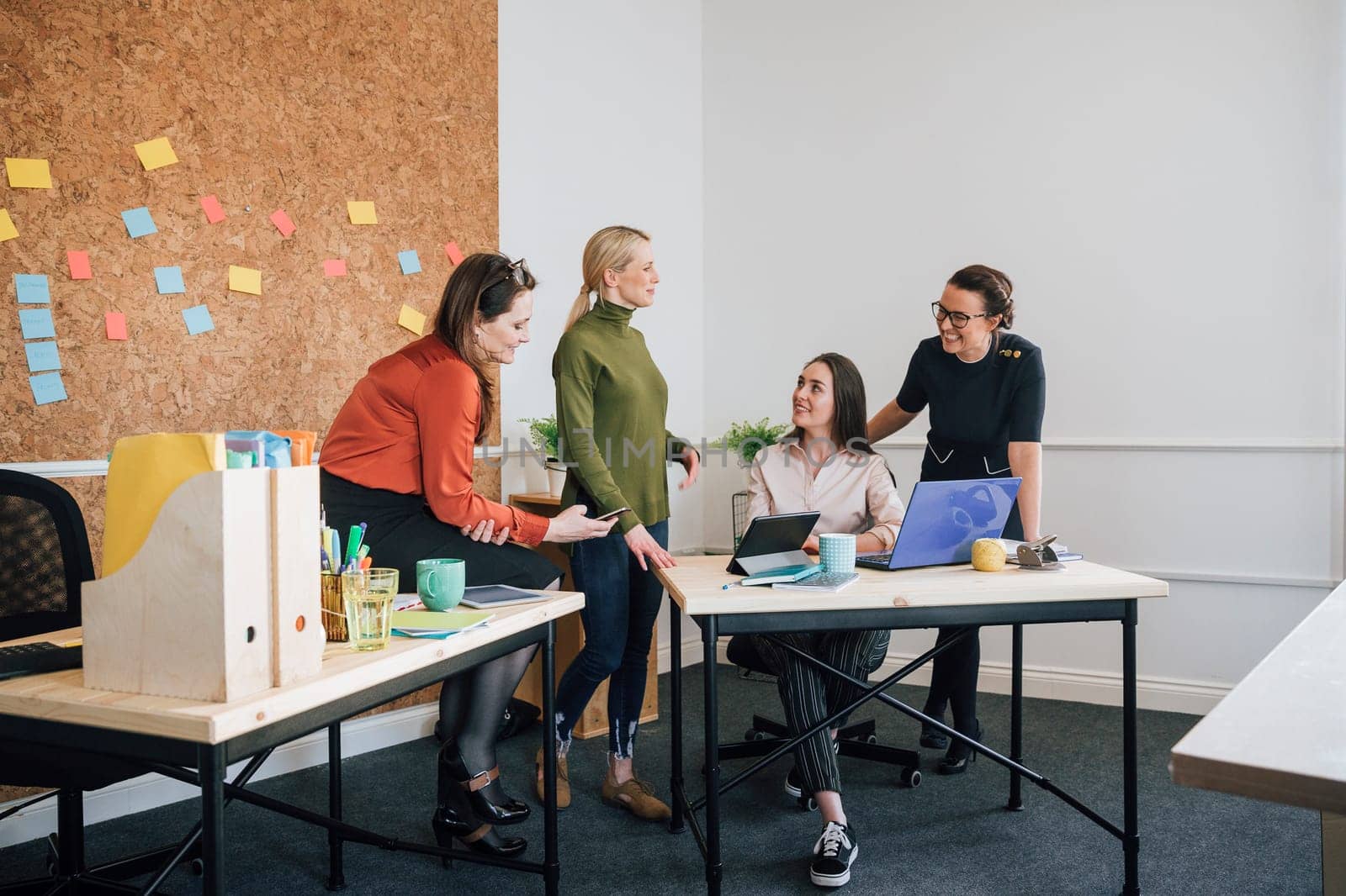 Women are working together in an office. They are talking as they use technology.