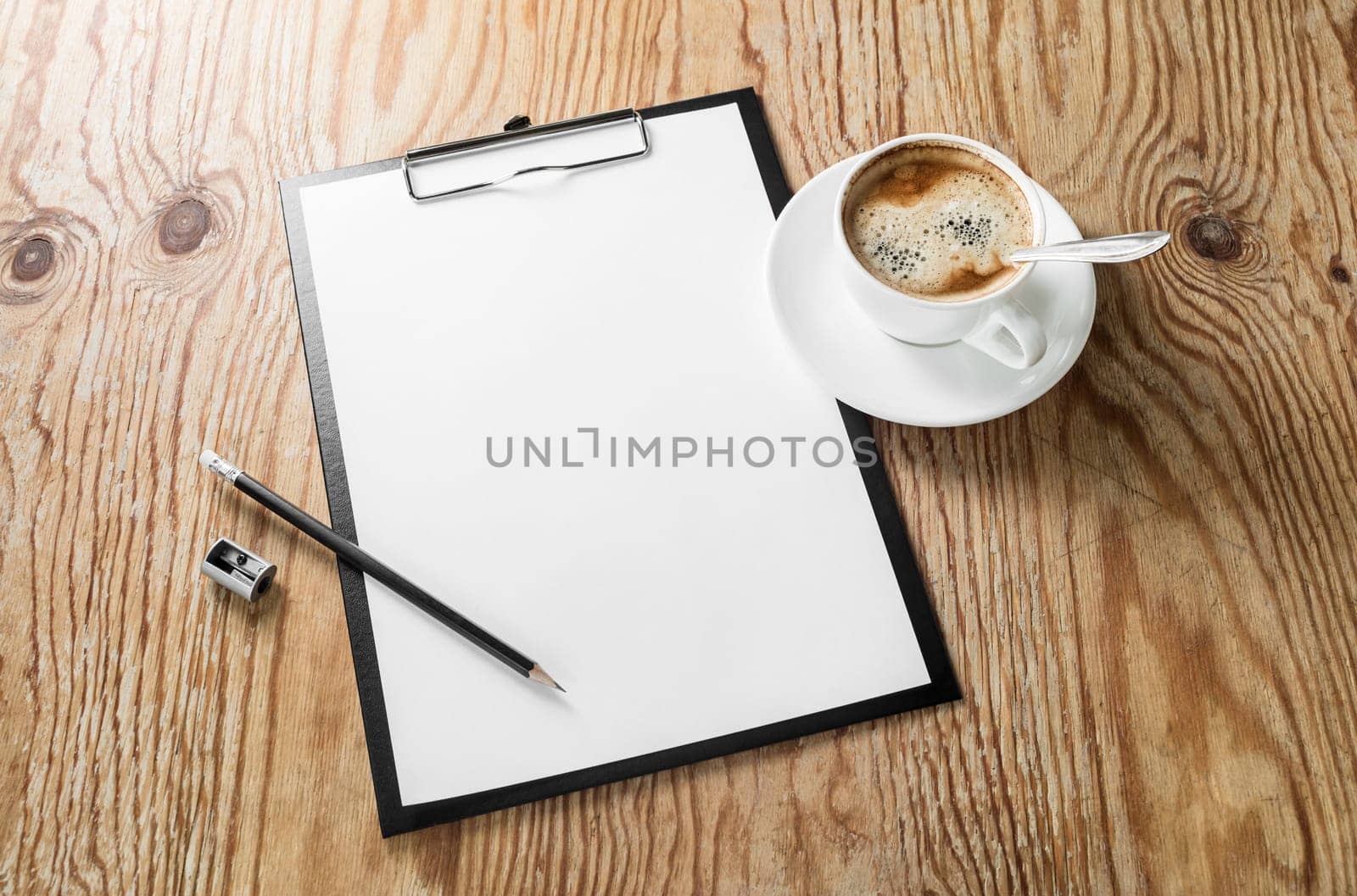 Photo of clipboard with a blank sheet of paper, coffee cup, pencil and sharpener on wooden background with plenty of copy space. Blank template for design presentations and portfolios. Responsive design mockup.