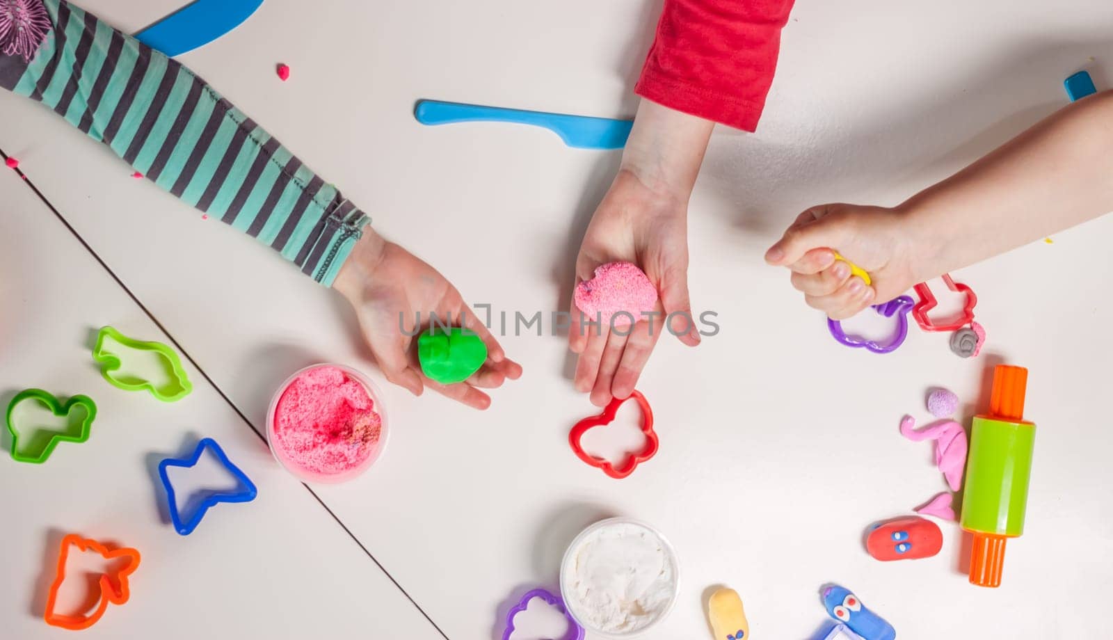 children hands playing with plasticine on white table top view