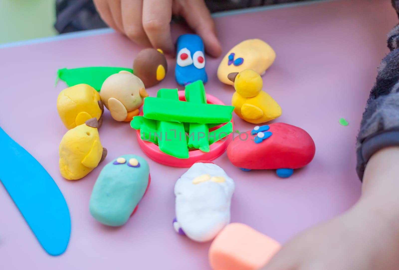 child hands playing with plasticine on blue table top view