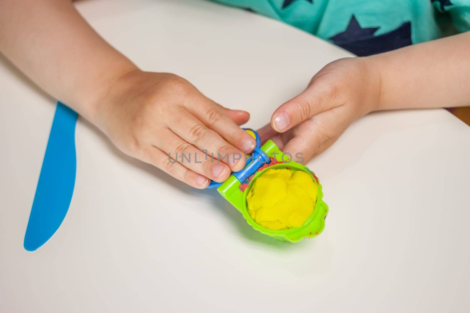 child hands playing with plasticine on blue table top view
