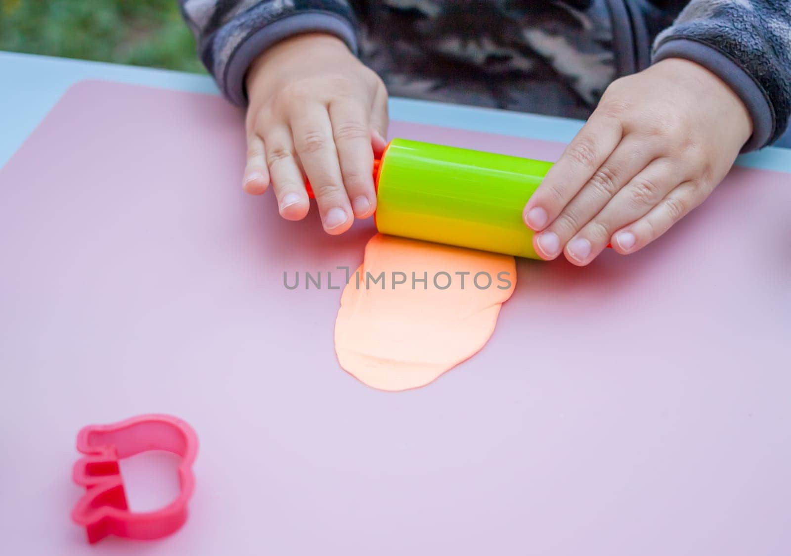 child hands playing with plasticine on blue table top view