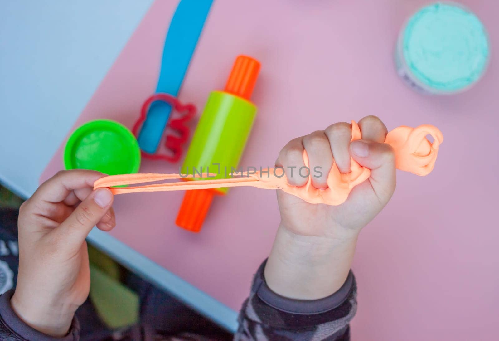 child hands keeping bright orange piece of plasticine above playing table