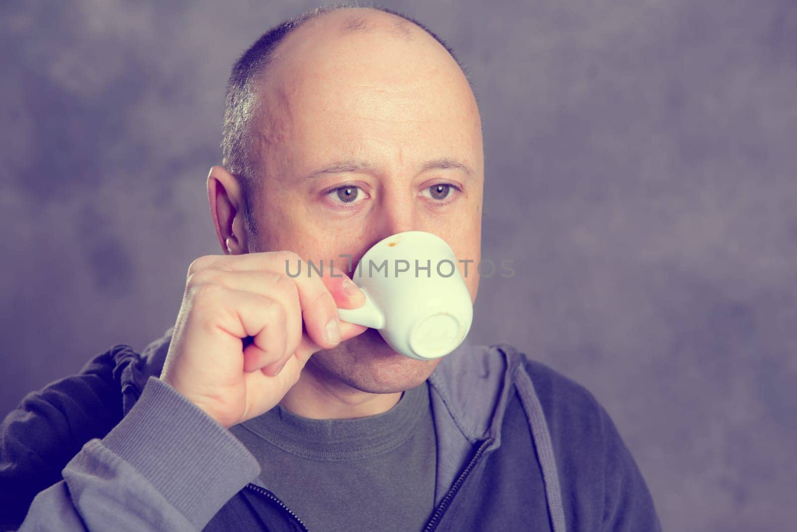 young baldheaded man drinking coffee in front of gray background