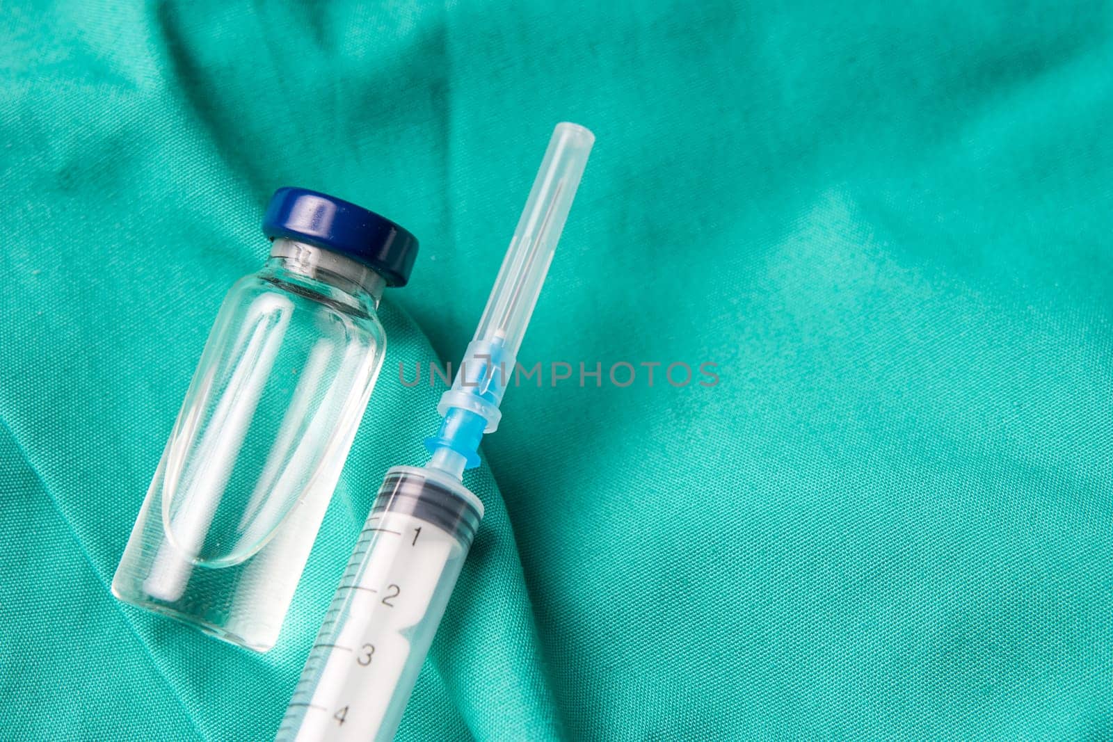 Medical syringe and vials lying on the hospital's green background. The background can be a textile part of a doctor or nurse's work uniform