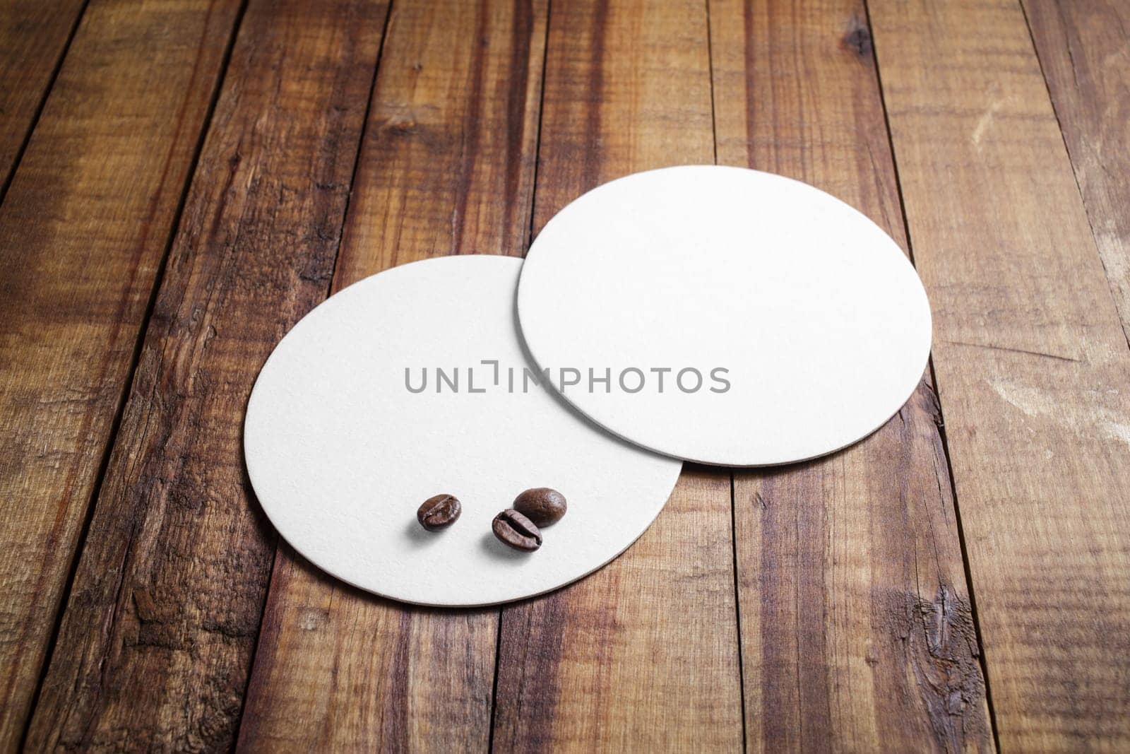 Two blank white beer coasters and coffee beans on vintage wooden table background.