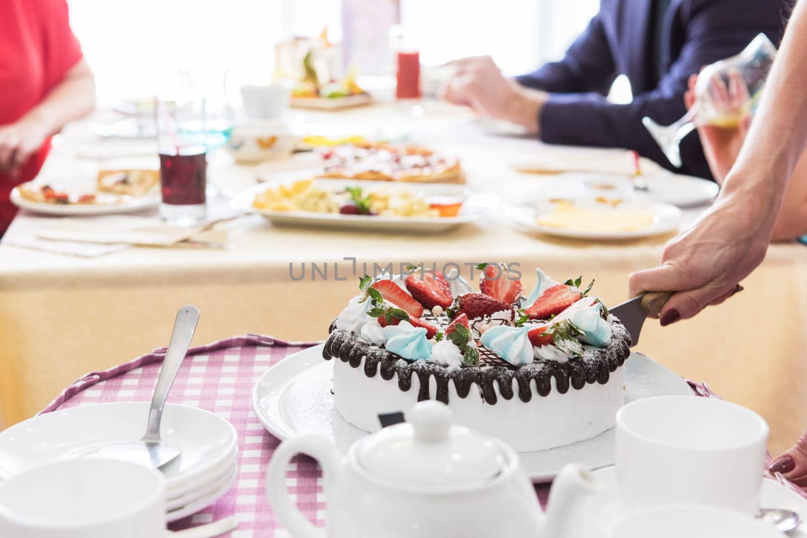 Tasty strawberry cream cake on checkered table, with tea set