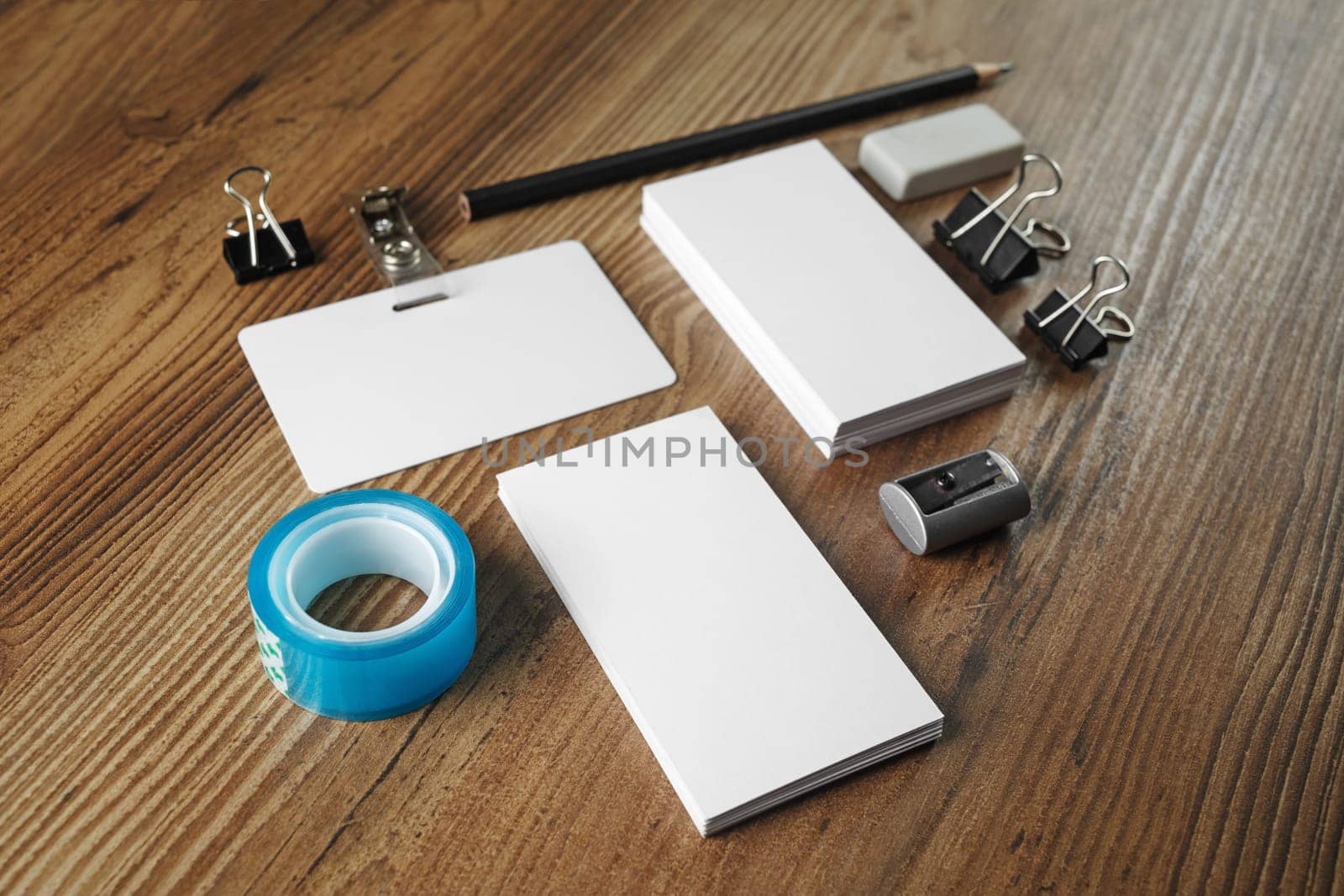 Photo of blank business cards, scotch tape, pencil, eraser, badge and sharpener on wood table background. Blank stationery for placing your design.