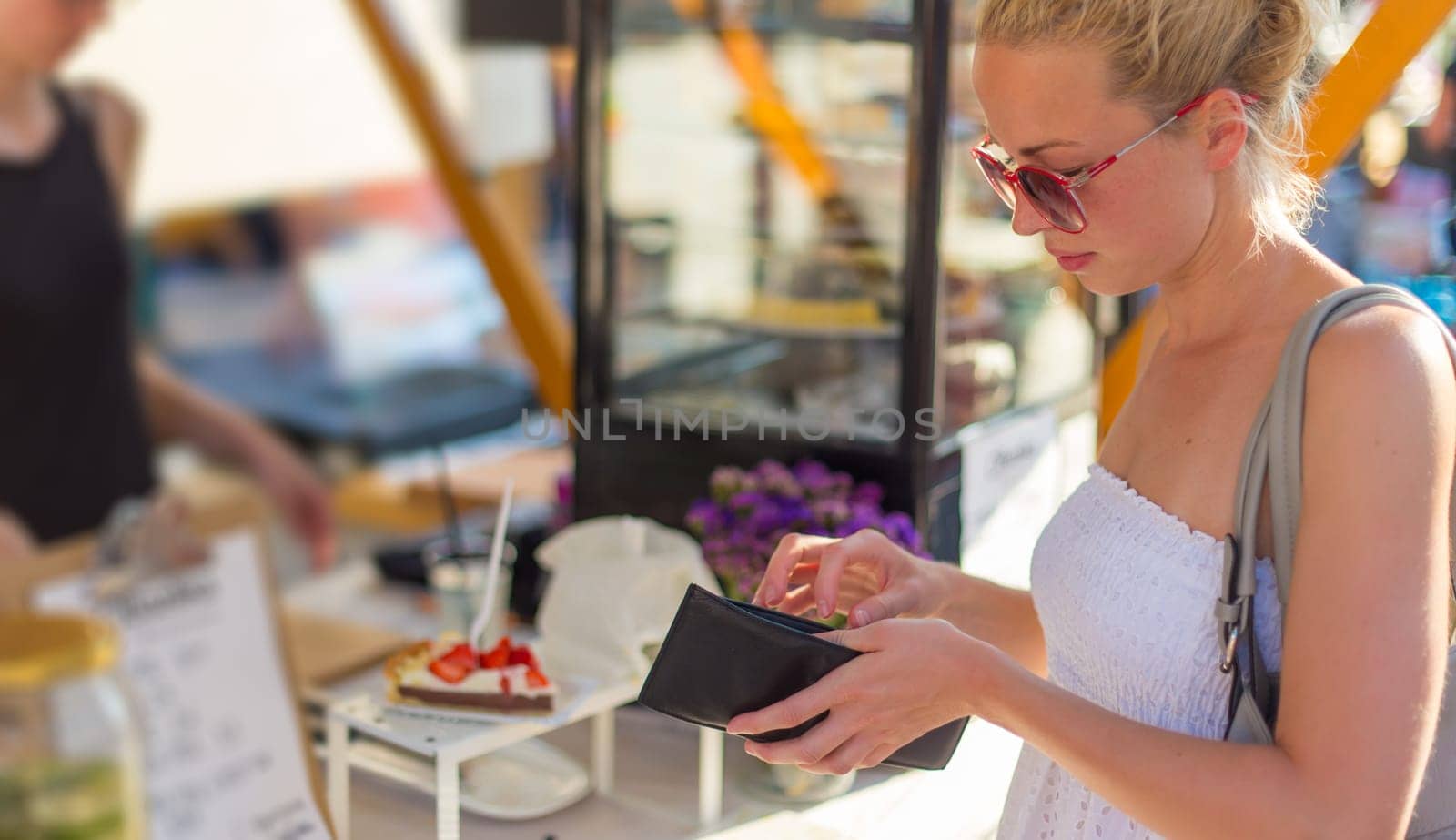 Beautiful blonde caucasian lady wearing white summer dress buying freshly prepared meal at a local street food festival. Urban international kitchen event in Ljubljana, Slovenia, in summertime.