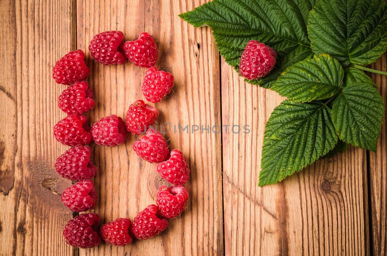 Letter B of raspberries with leaves on a wooden surface, close-up