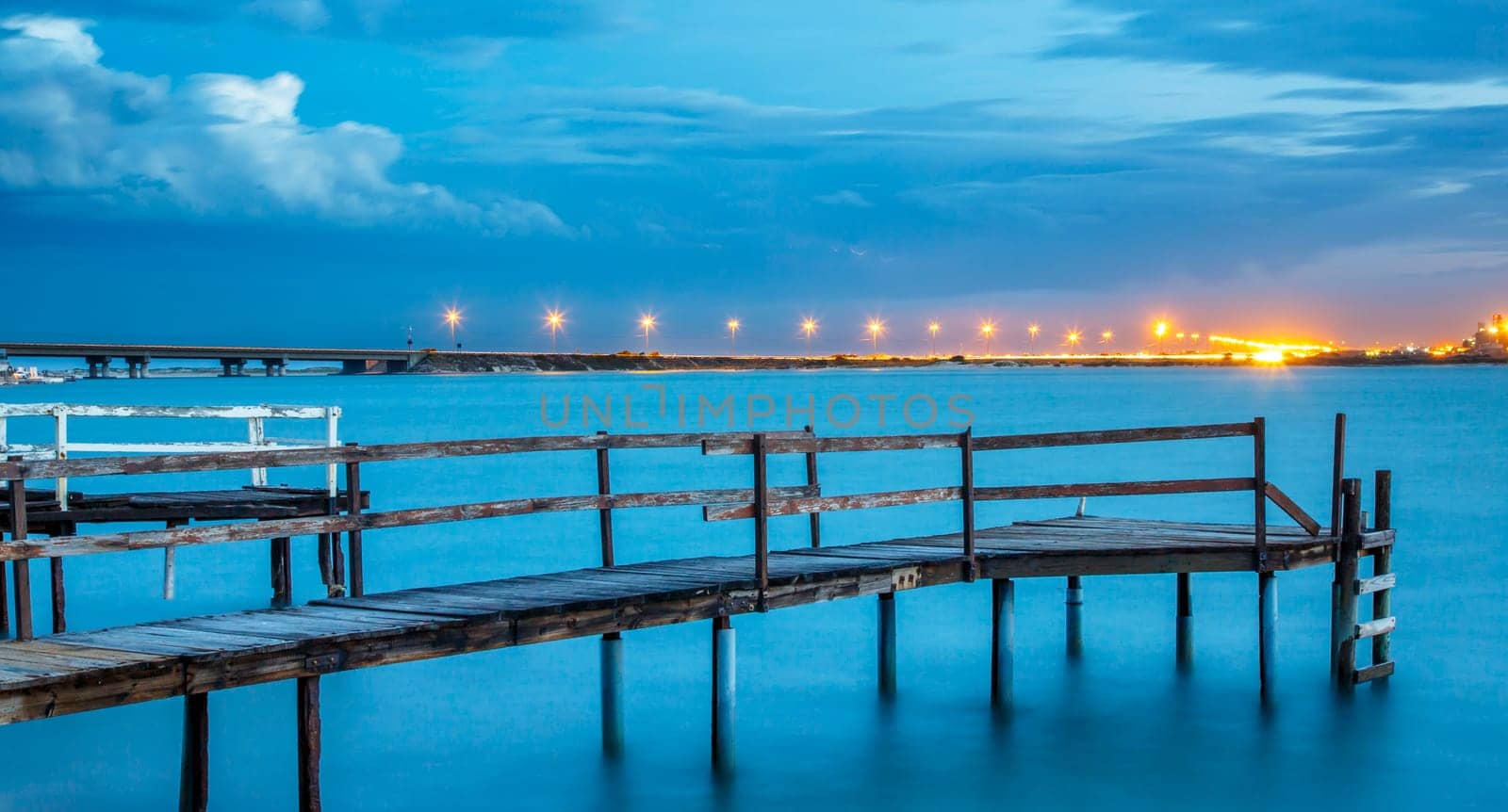 Long exposure of an old jetty on a river with city lights in the background