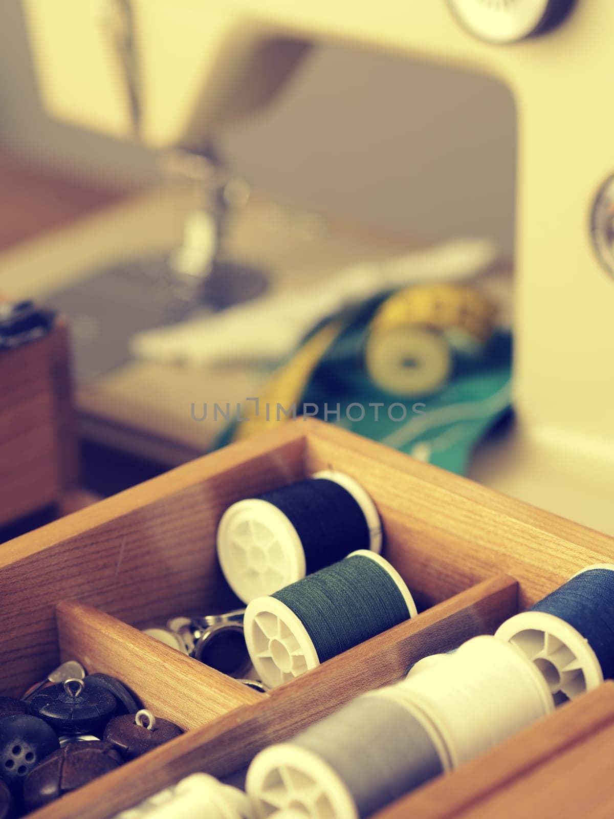 Old vintage sewing utensils in a wooden box, sewing machine in background, retro film toned image