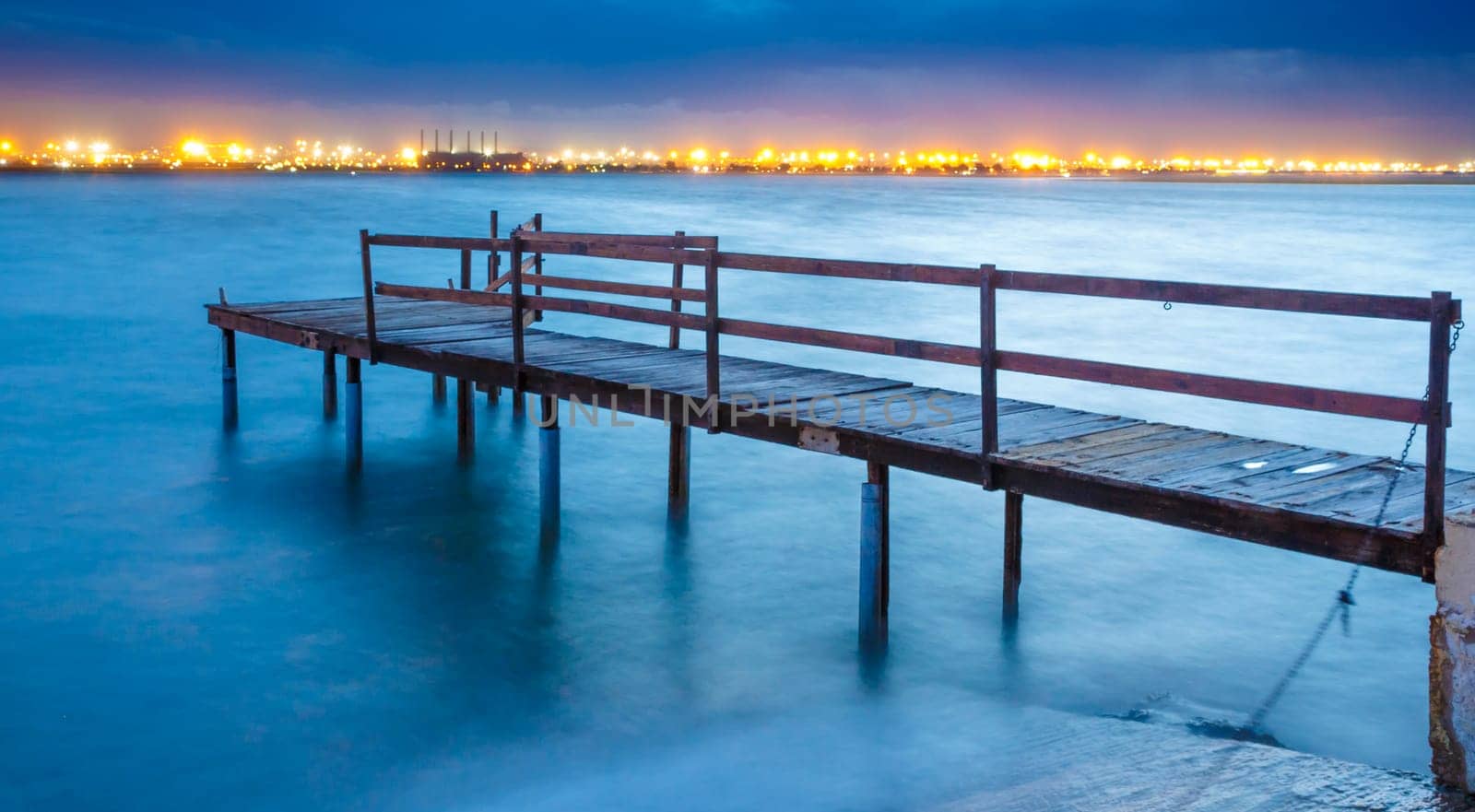 Long exposure of an old jetty on a river with city lights in the background