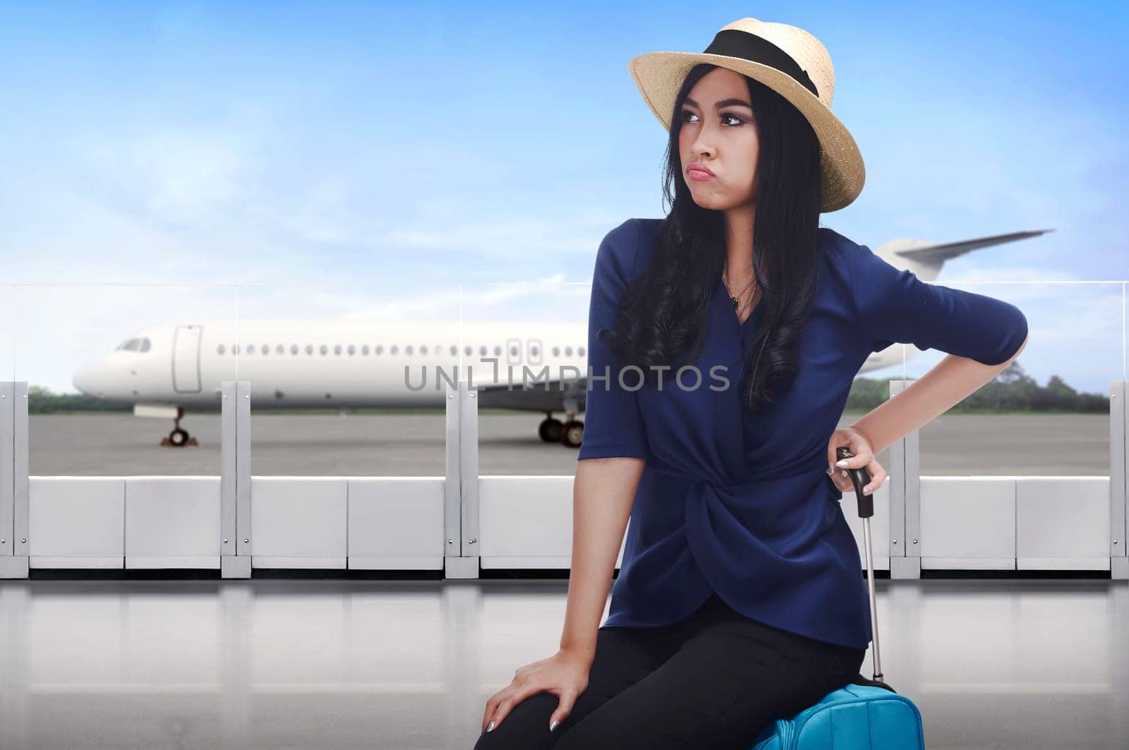 Portrait of asian traveler woman with unhappy face sitting on suitcase in the airport