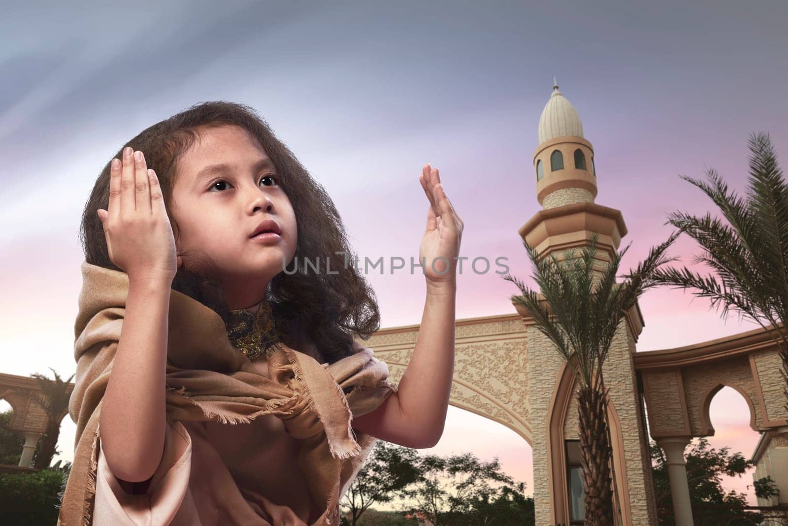 Little asian muslim girl raising hand and praying with sunset background