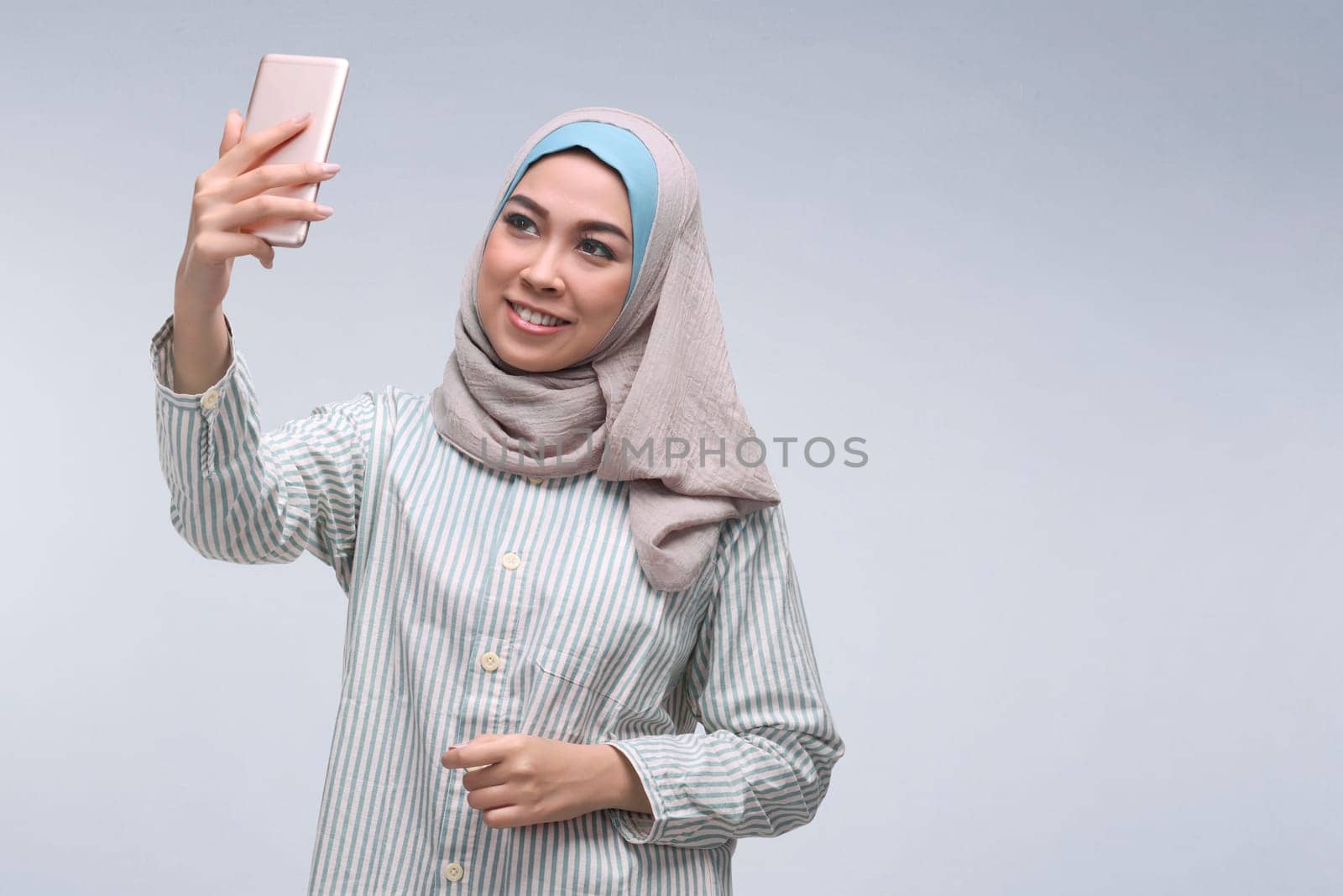 Young asian muslim woman posing talking selfie with mobile phone over dark background