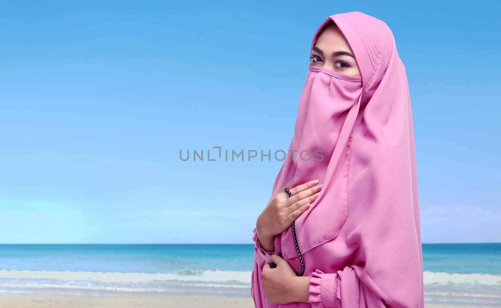 Portrait of asian muslim woman with niqab holding prayer beads on the beach
