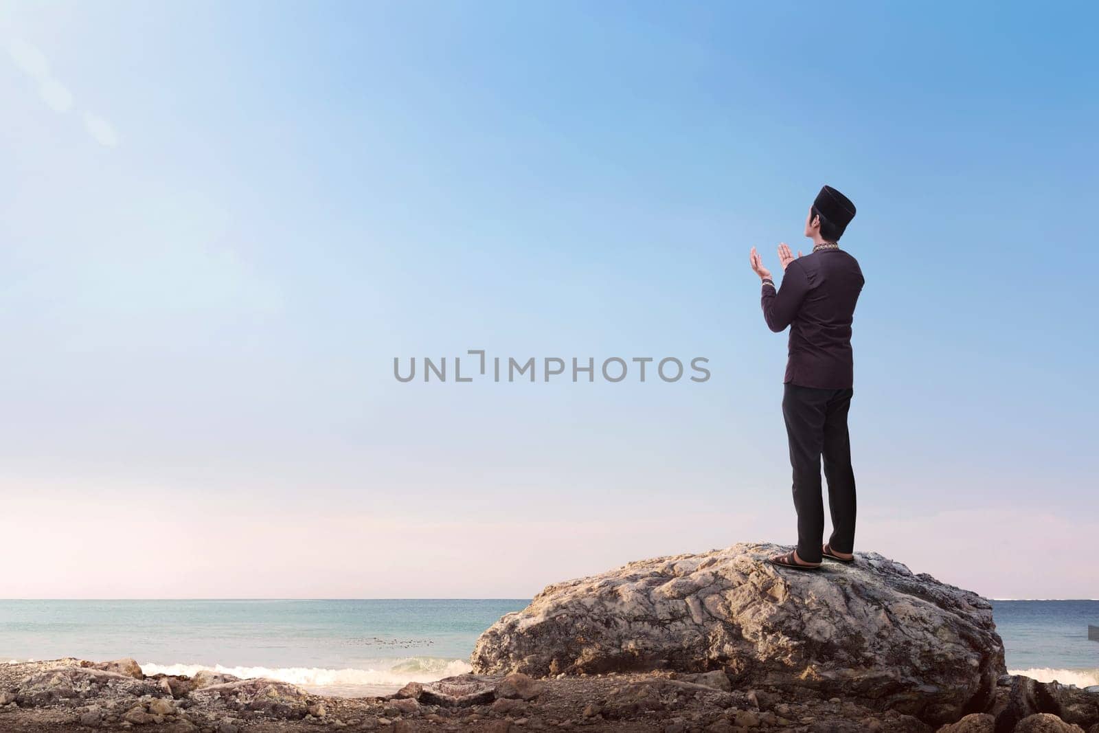 Religious asian muslim man raising hand and praying with blue sky background