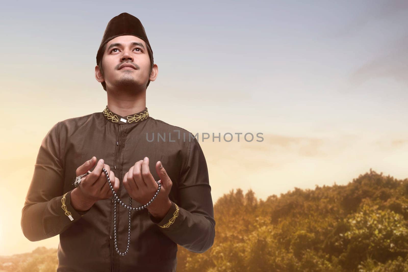 Handsome asian muslim man holding prayer beads and praying during sunset