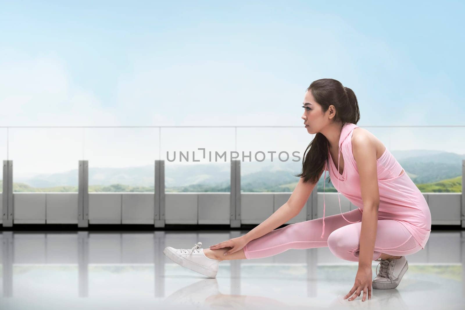 Portrait of asian woman in sportswear doing stretching while kneeling in front of window at gym
