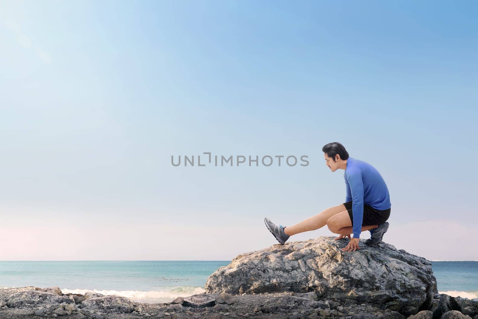 Portrait of asian fitness man stretching legs before jogging on the beach