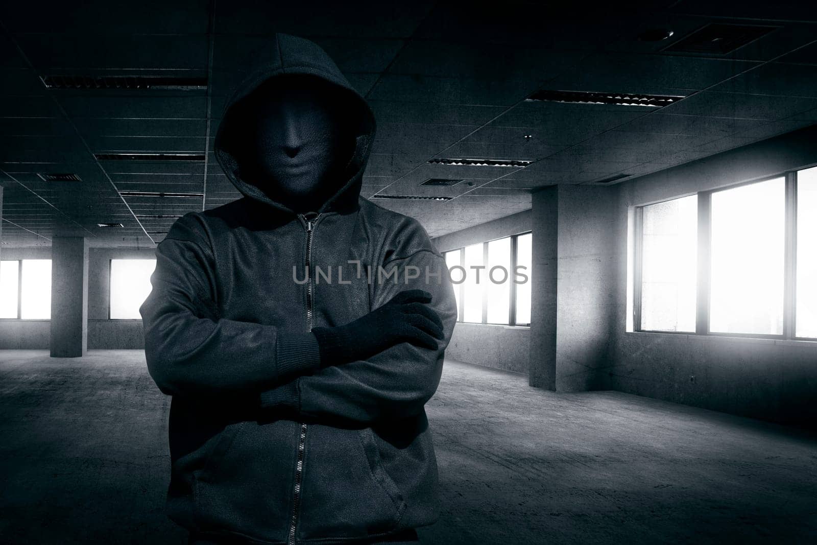 Hooded man with mask standing alone in the empty dark room