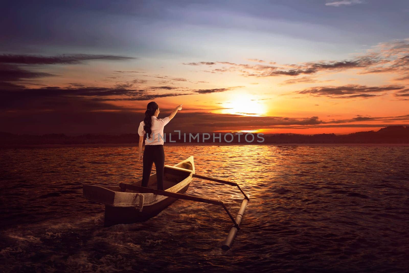 Beautiful asian business woman standing and pointing to the sun on the boat at sunset