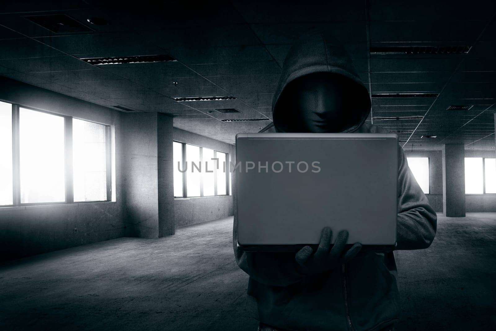 Hacker with mask using laptop on the empty dark room