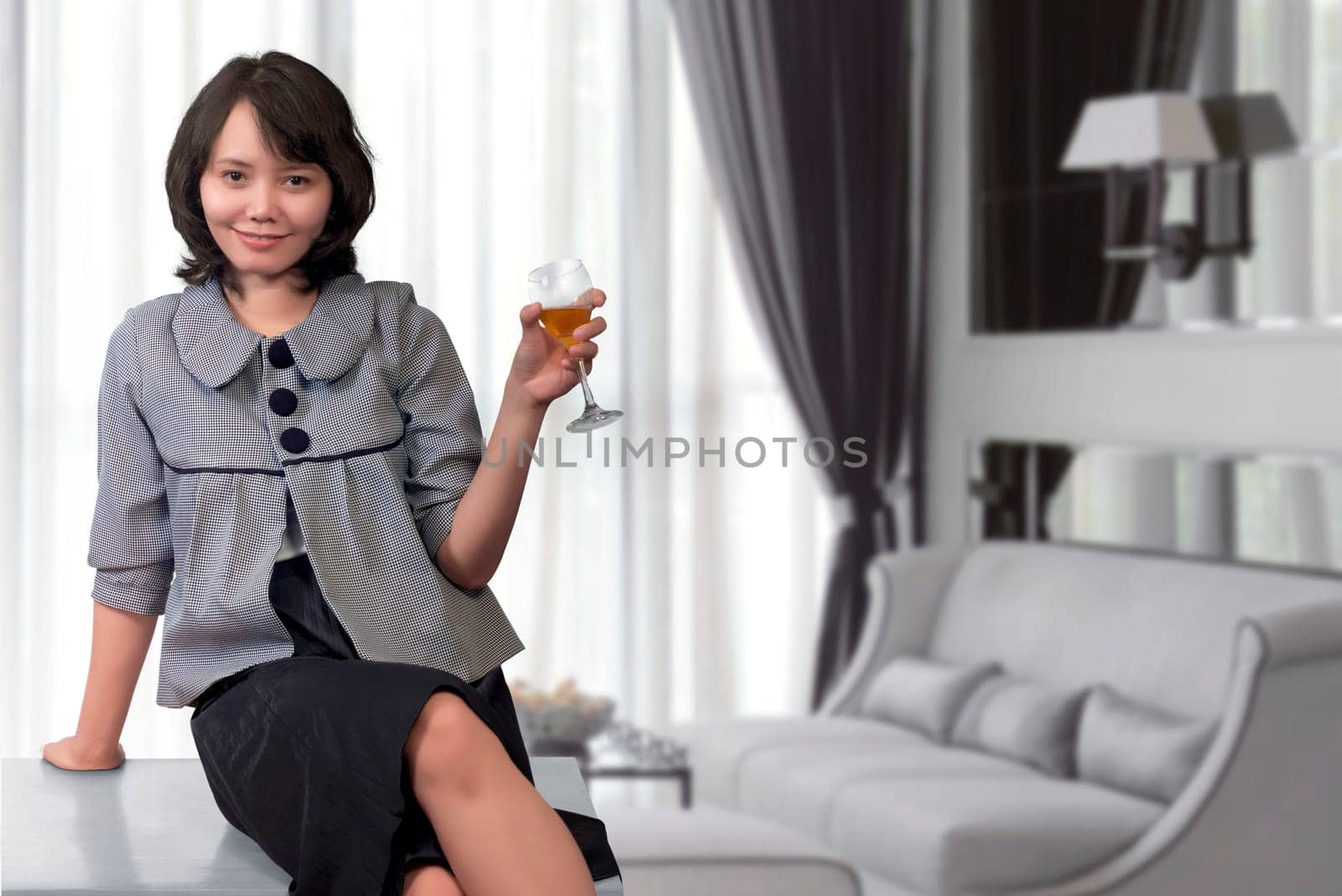 Relaxed asian woman sitting on desk with glass of wine at home