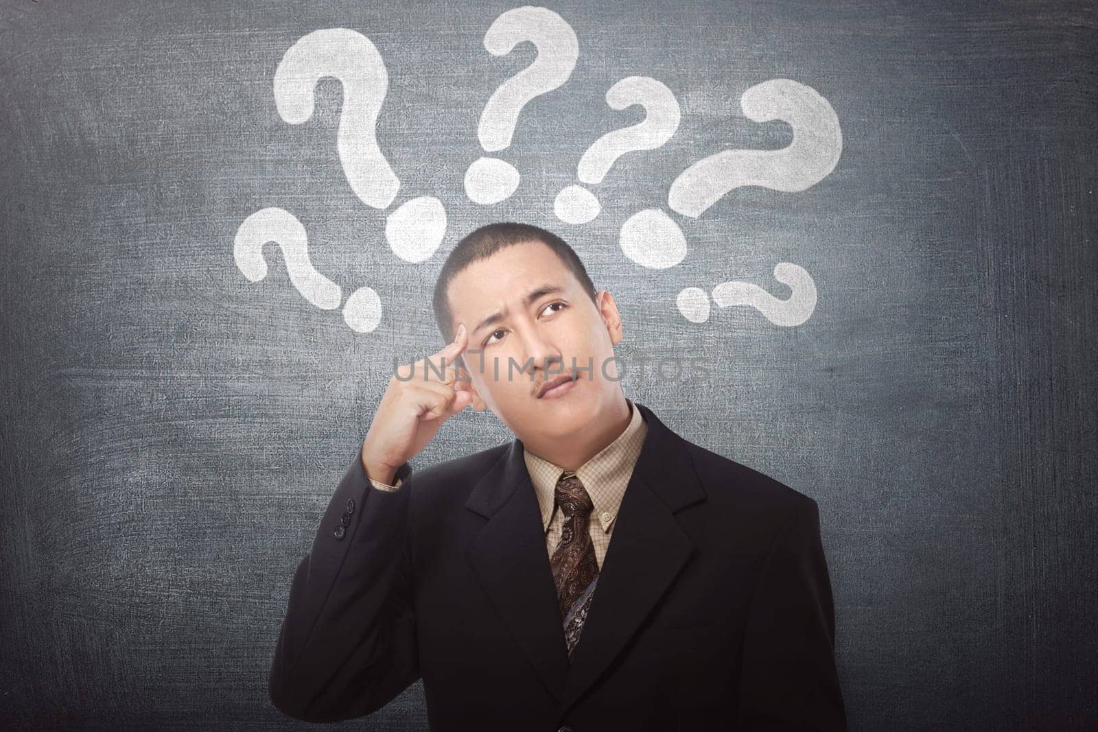 Young asian businessman confused with question marks above his head on black background