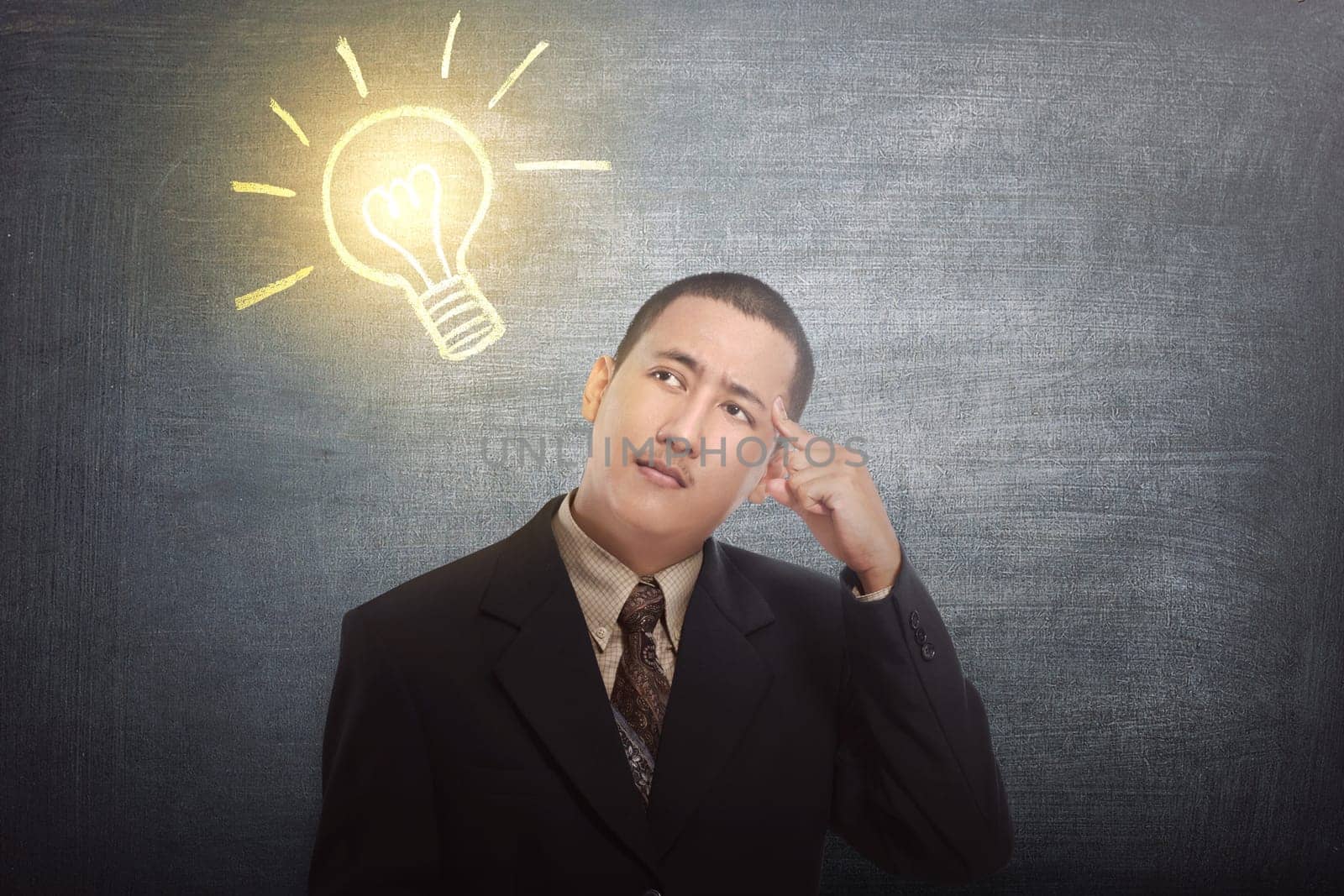 Thinking asian businessman got idea with bright light bulb over his head on black background